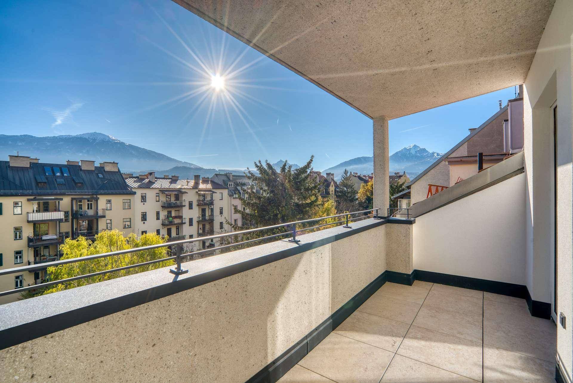 Geräumiger Balkon mit weitreichendem Blick über die Stadt und die umliegende Berglandschaft an einem sonnigen Tag.