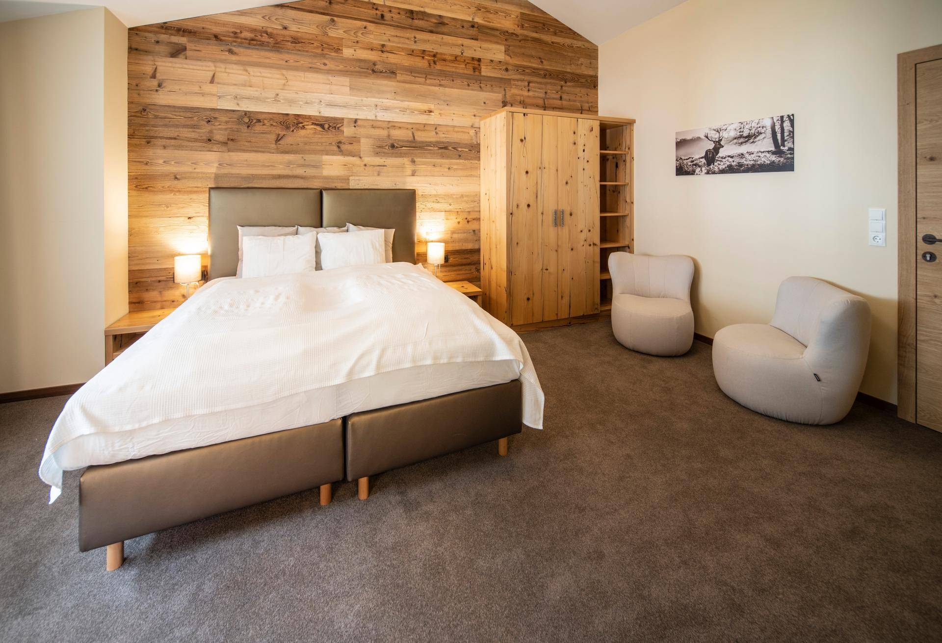 Helles Schlafzimmer mit Holzwand, Teppichboden und gemütlichen Sesseln unter Dachschräge.