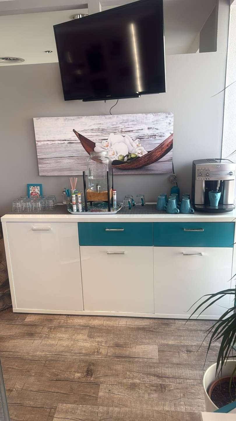 Erfrischungsbereich mit Kaffeemaschine, Schränken und einem an der Wand montierten Fernseher.