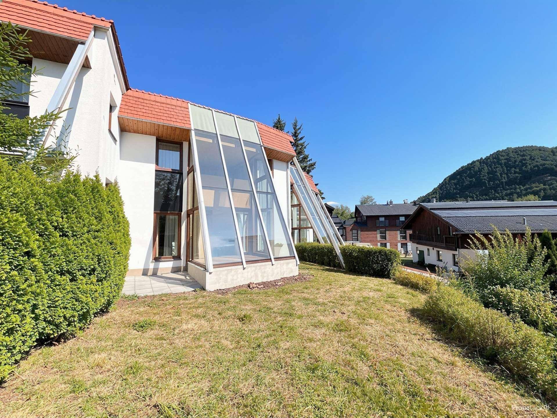 Außenansicht eines Hauses mit großer Glasfassade, umgeben von einem grünen Garten und Bäumen.