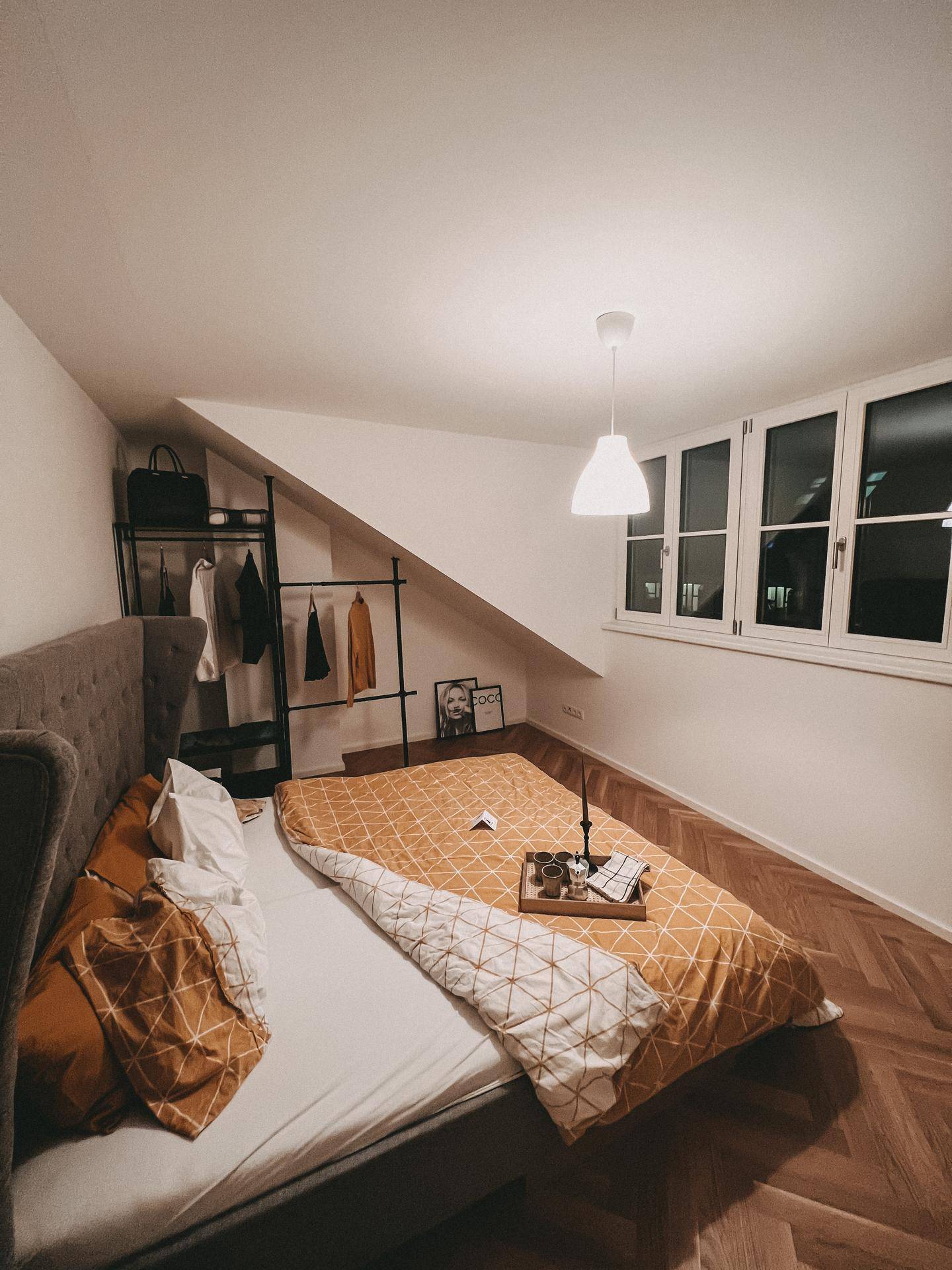 Gemütliches Schlafzimmer mit Doppelbett, Fischgrätparkett und schrägen Wänden unter dem Dach.