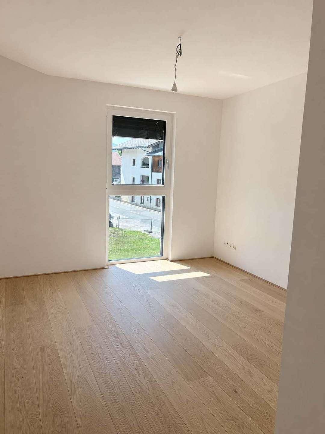 Helles Zimmer mit Holzboden und großem Fenster, ideal als Schlaf- oder Arbeitszimmer.
