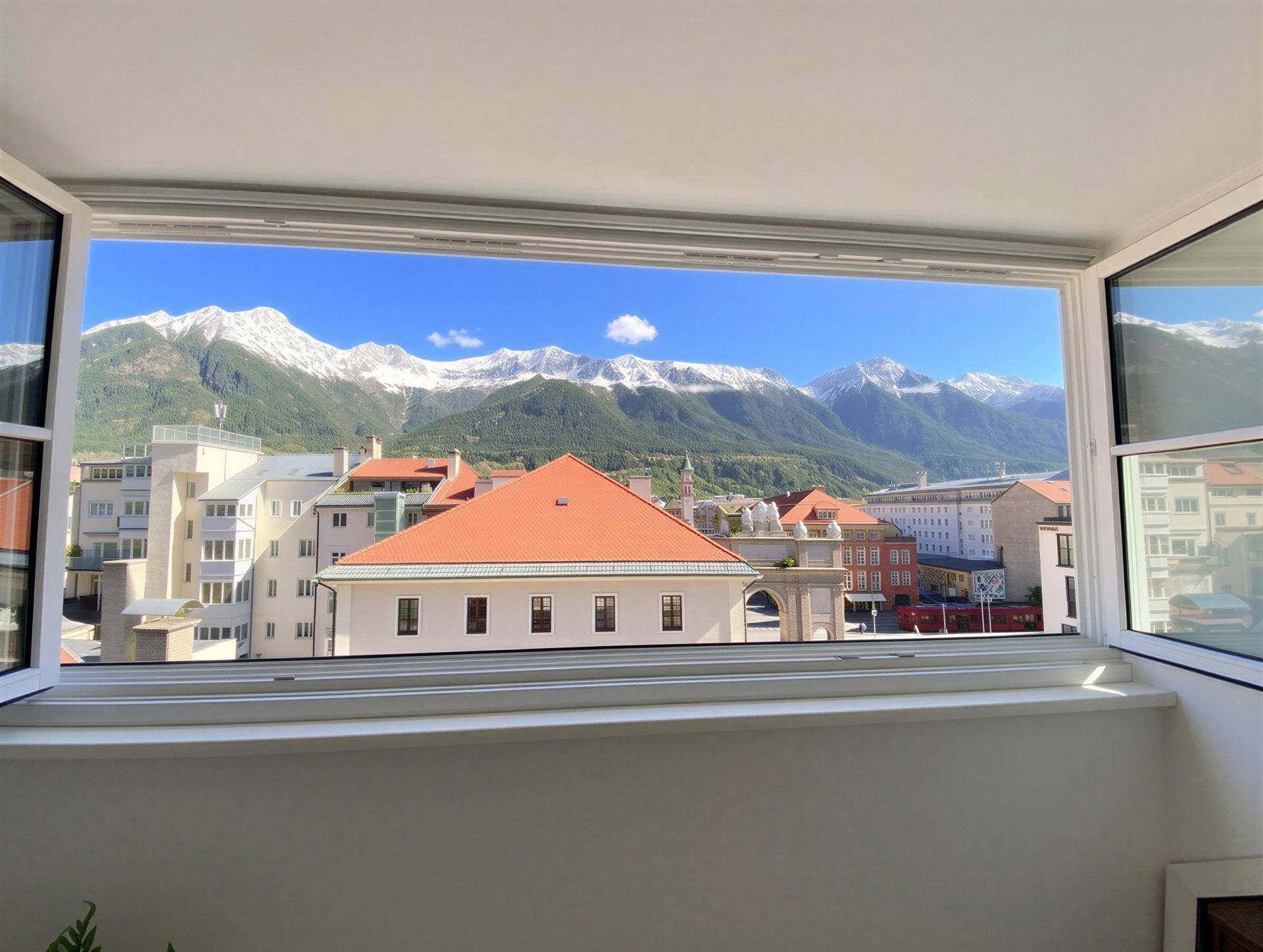 Spektakulärer Bergblick von einem Balkon über die Dächer der Stadt an einem sonnigen Tag.