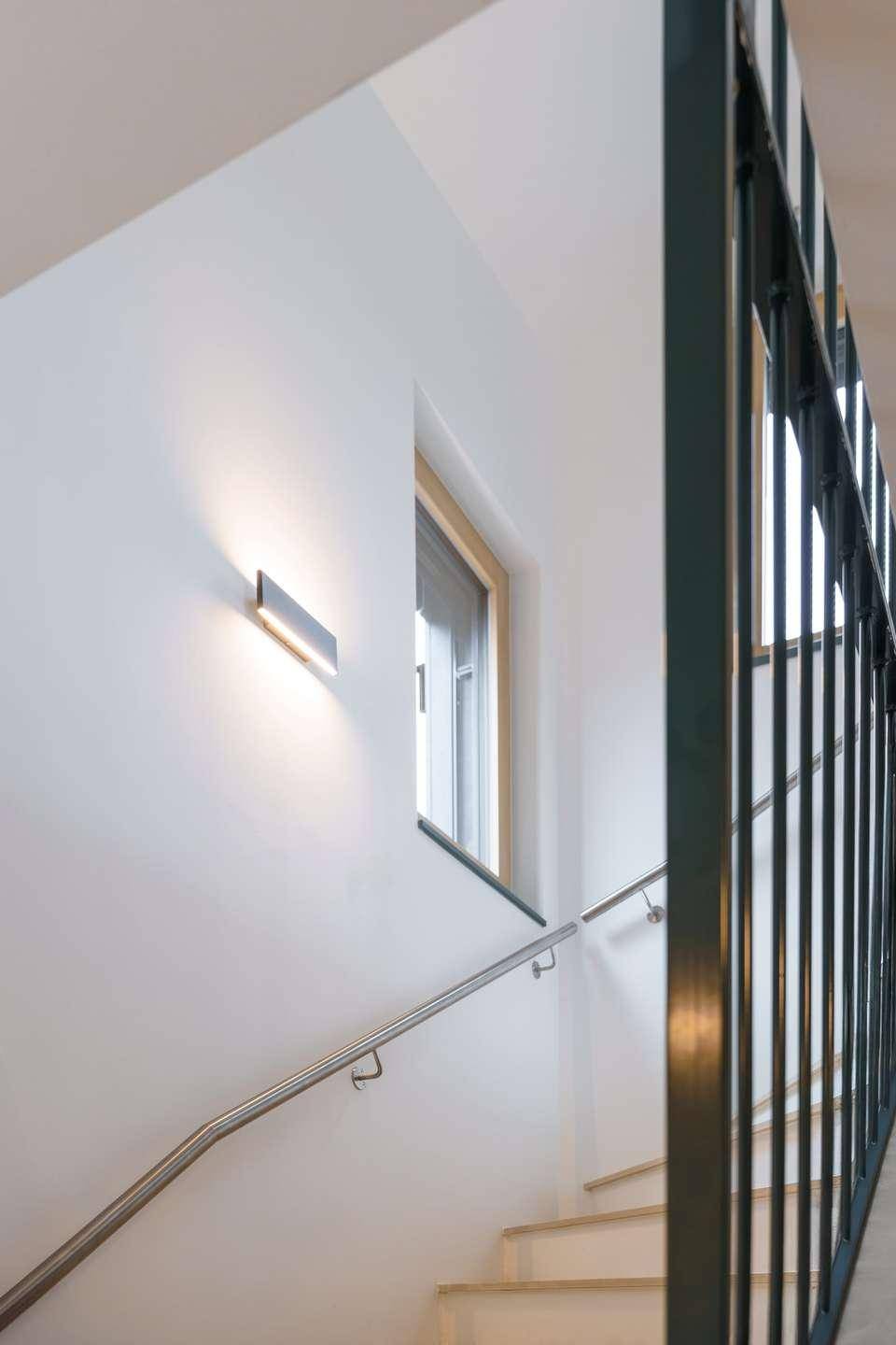 Treppenaufgang mit weiß gestrichenen Wänden, modernem Geländer und Wandleuchte.