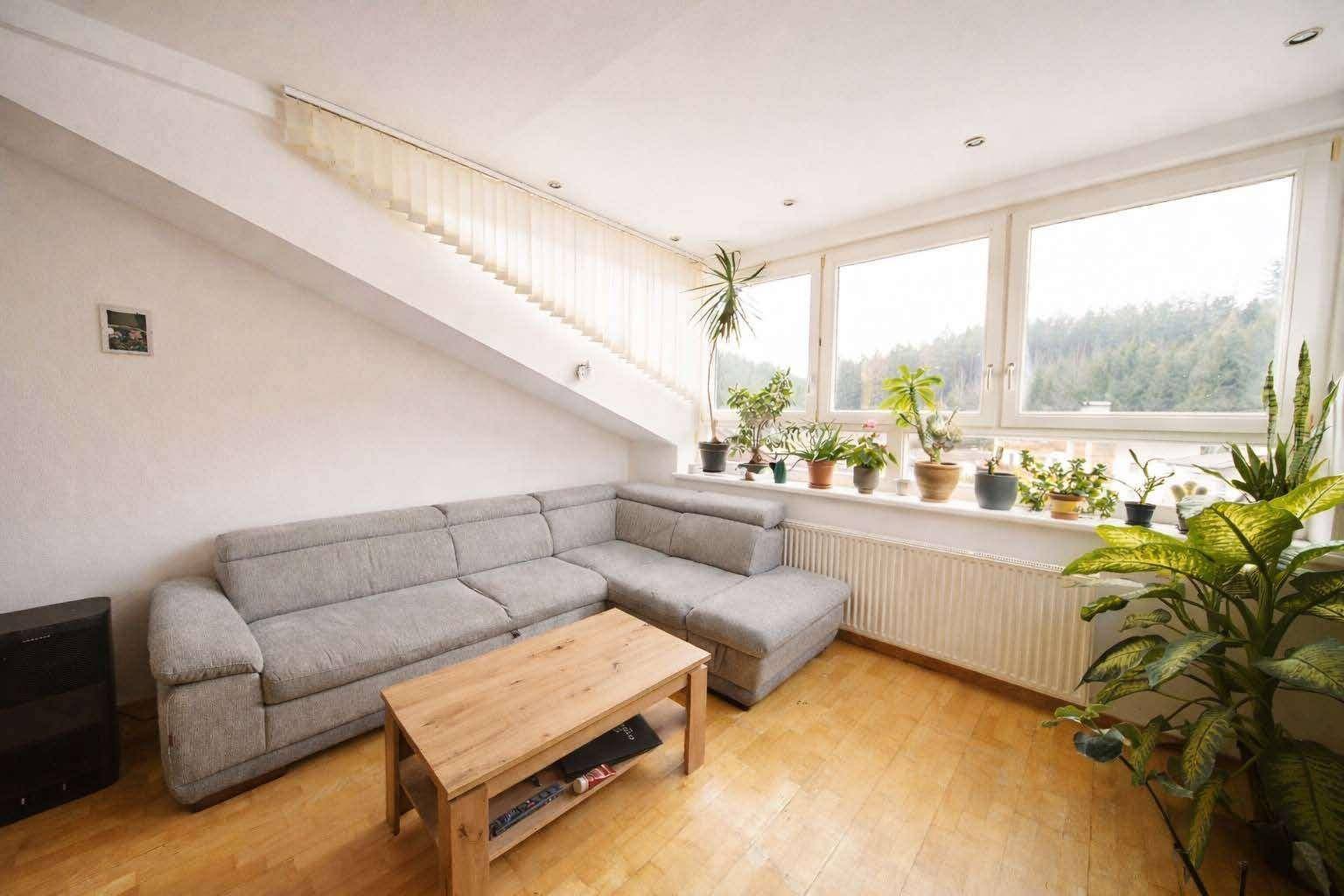 Heller Wohnraum mit Ecksofa, Couchtisch und breiter Fensterfront, die viel Licht hereinlässt.