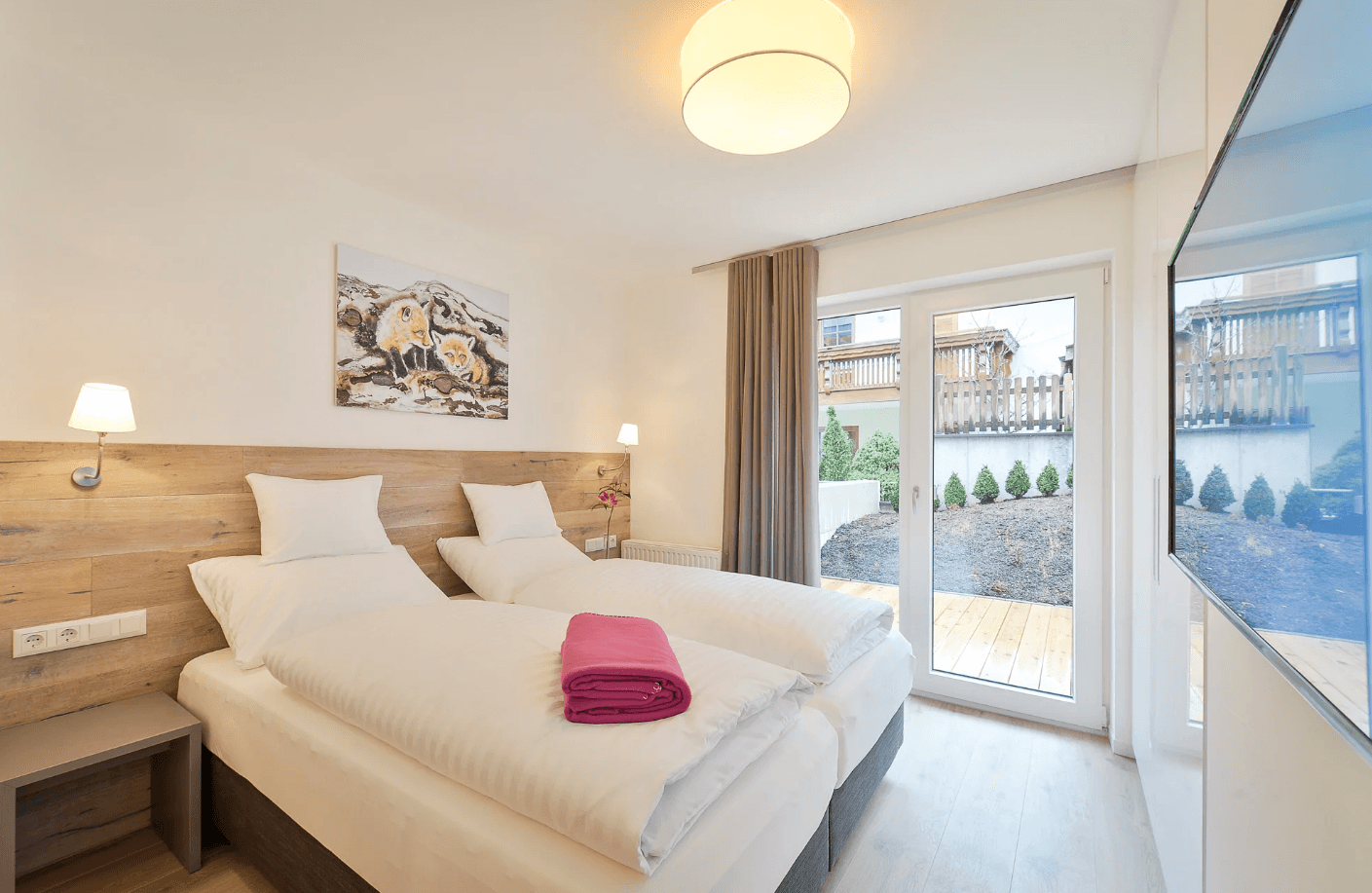 Helles Schlafzimmer mit zwei Einzelbetten, Holzboden und Zugang zu einem Außenbereich.
