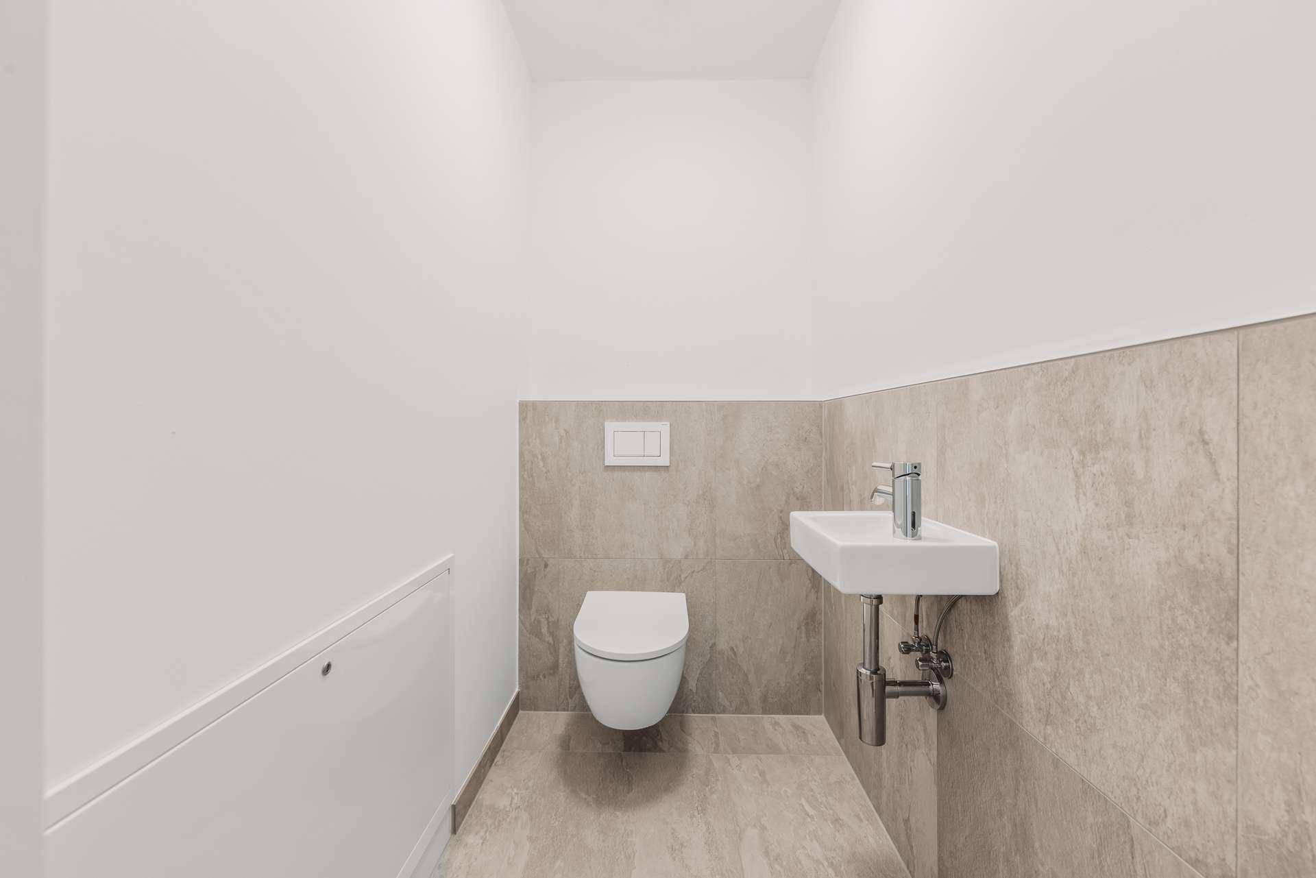 Modernes Gäste-WC mit Wand-WC, kleinem Waschbecken und hellen Fliesen.