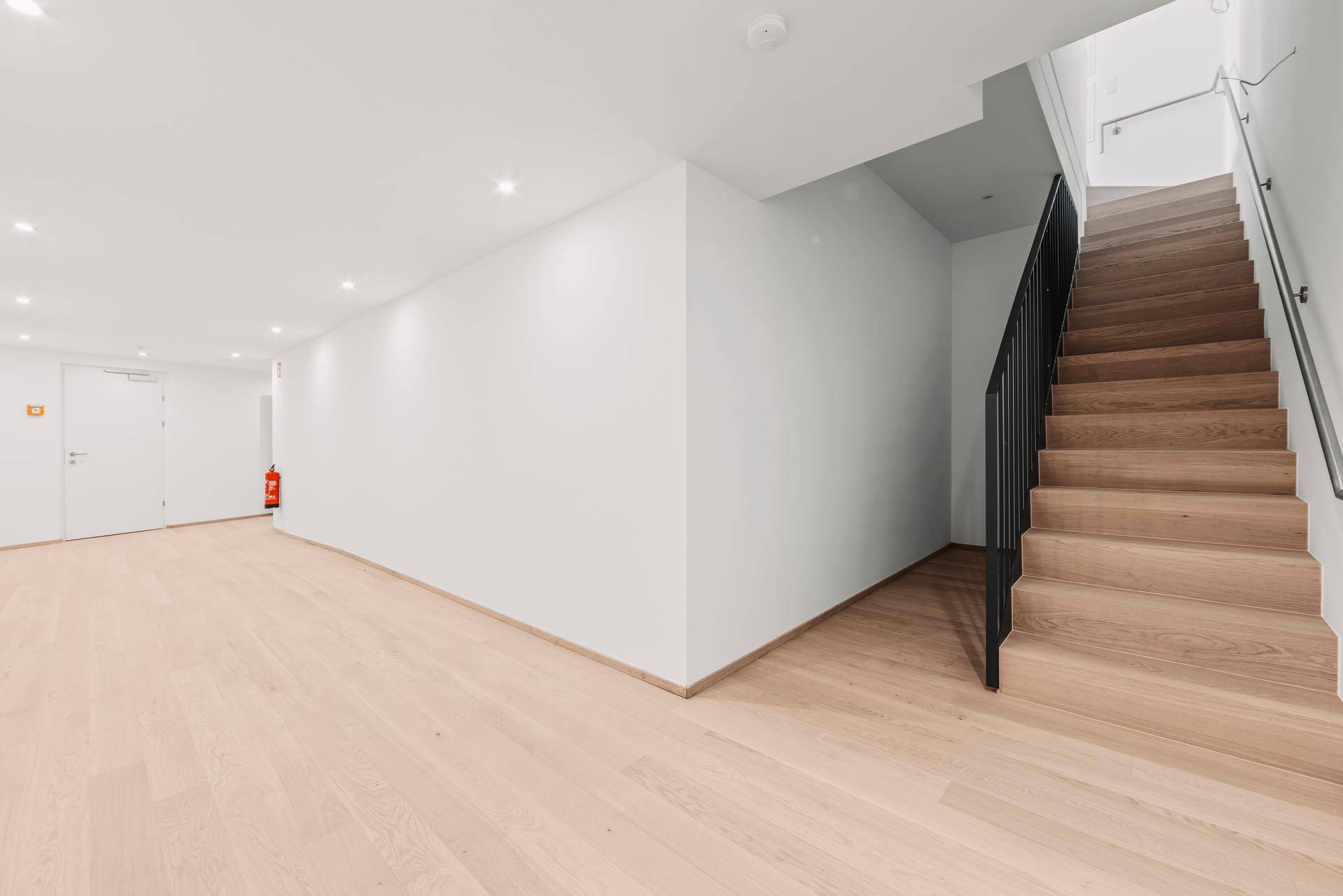 Heller Kellerflur mit Holztreppe, Parkettboden und moderner Beleuchtung.