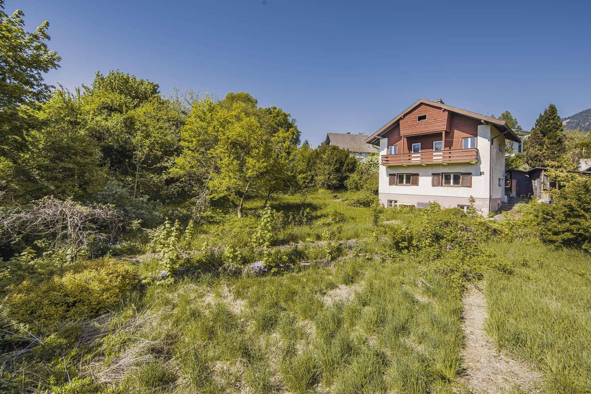 Freistehendes Haus mit Holzfassade und Balkonen, umgeben von einem großen, naturbelassenen Grundstück.