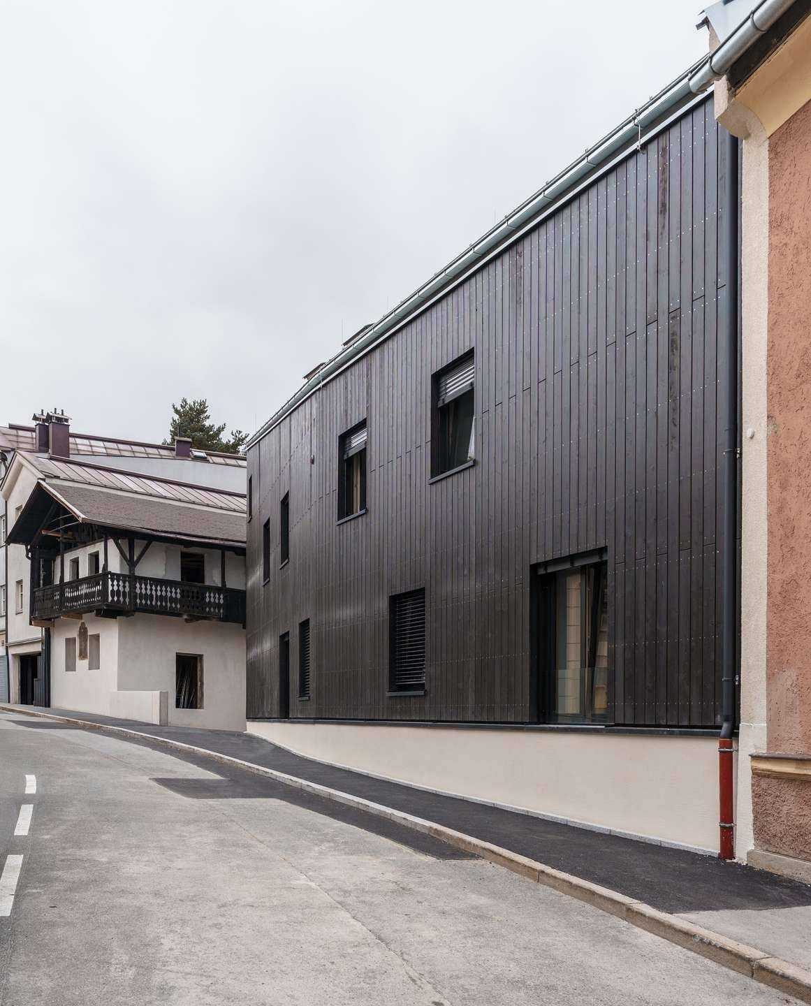 Lange Fassade des modernen Gebäudes mit dunkler Holzverkleidung entlang einer Straße.