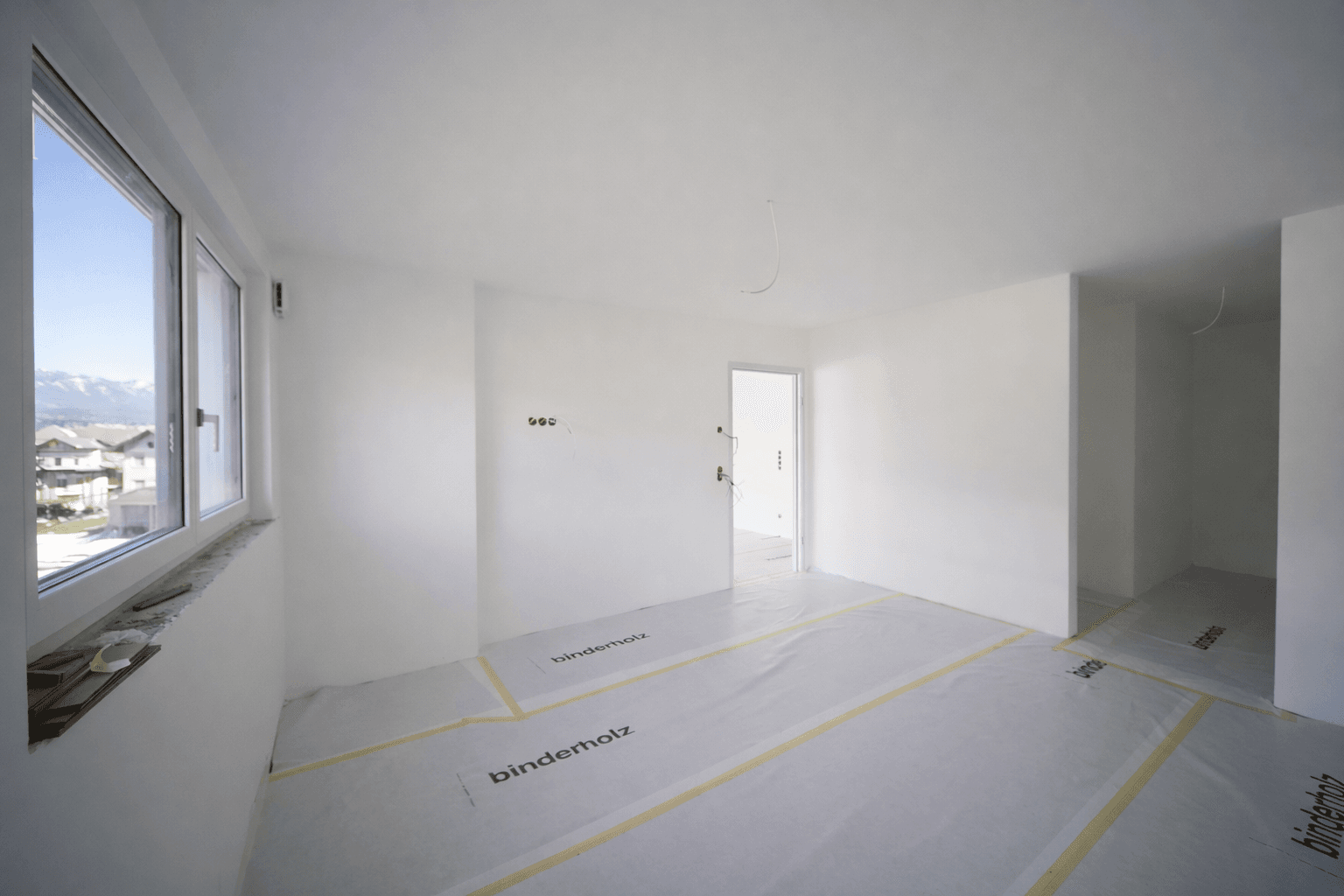 Helles Schlafzimmer im Rohbau mit Fenster und Blick auf die Umgebung.