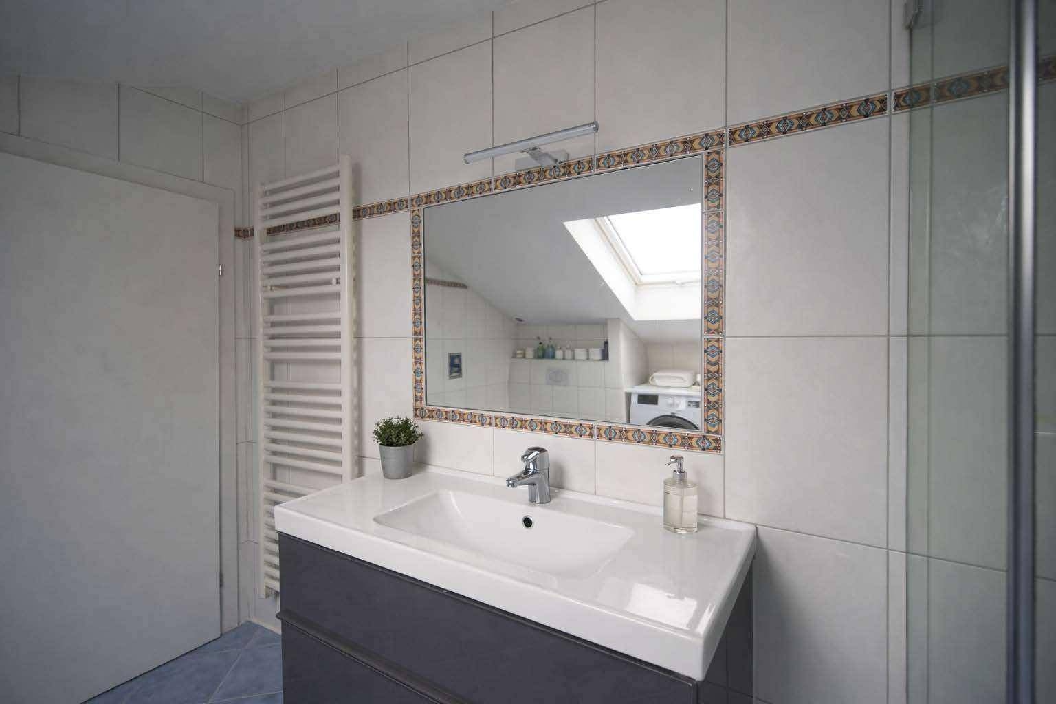 Badezimmer mit Waschbecken, Spiegel, beheiztem Handtuchhalter und Dachfenster.