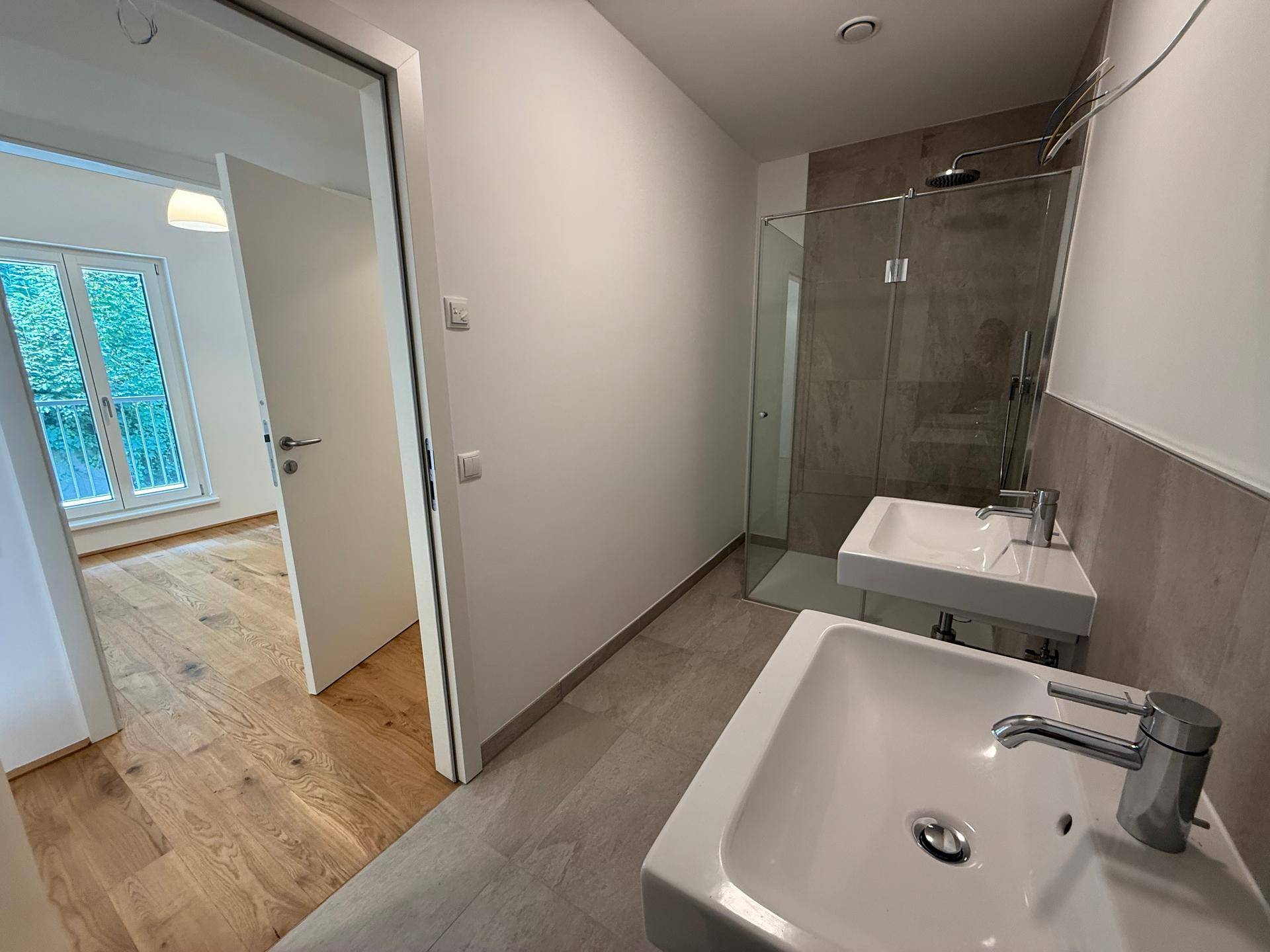 Modernes Badezimmer mit zwei Waschbecken, Dusche und hellen Fliesen.