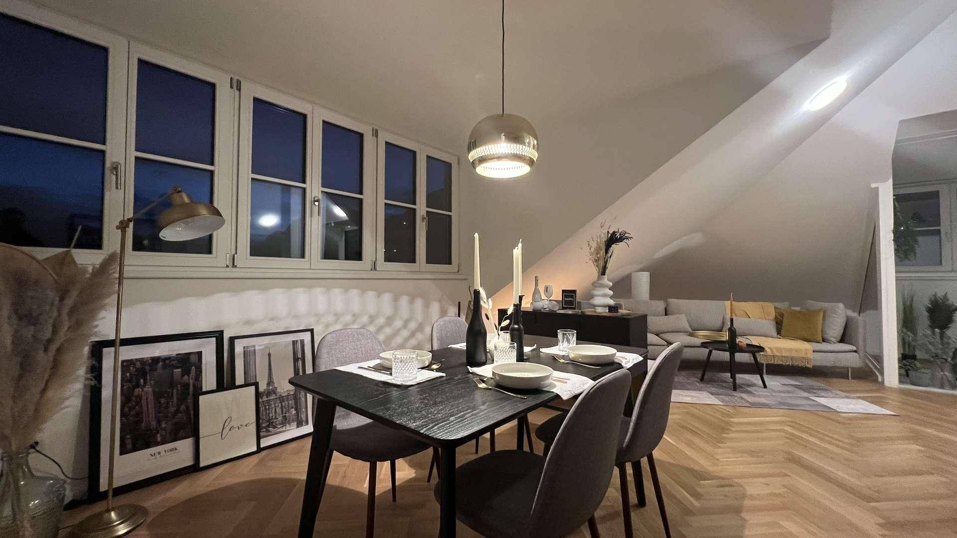 Gemütlicher Wohn-Essbereich am Abend mit Esstisch, Sofa und schrägen Decken.
