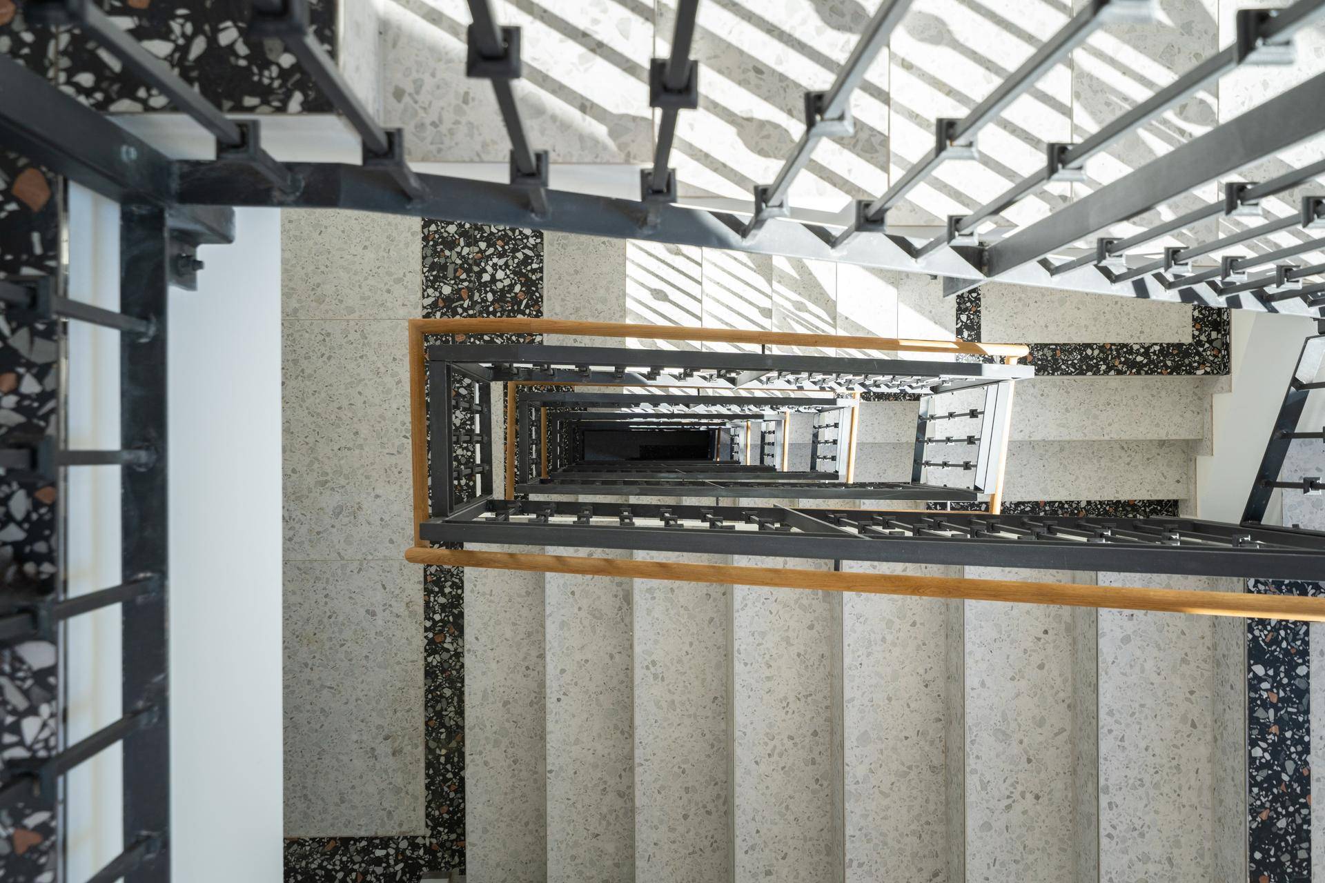 Moderner Treppenaufgang mit Terrazzoboden und Metallgeländer, von oben fotografiert, mit viel Tageslicht.