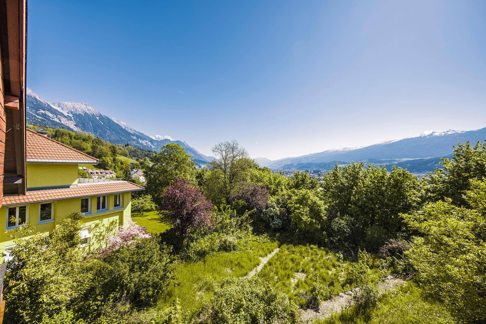 Gelbes Gebäude mit weitem Blick über grüne Landschaft und die majestätischen Berge in der Ferne.
