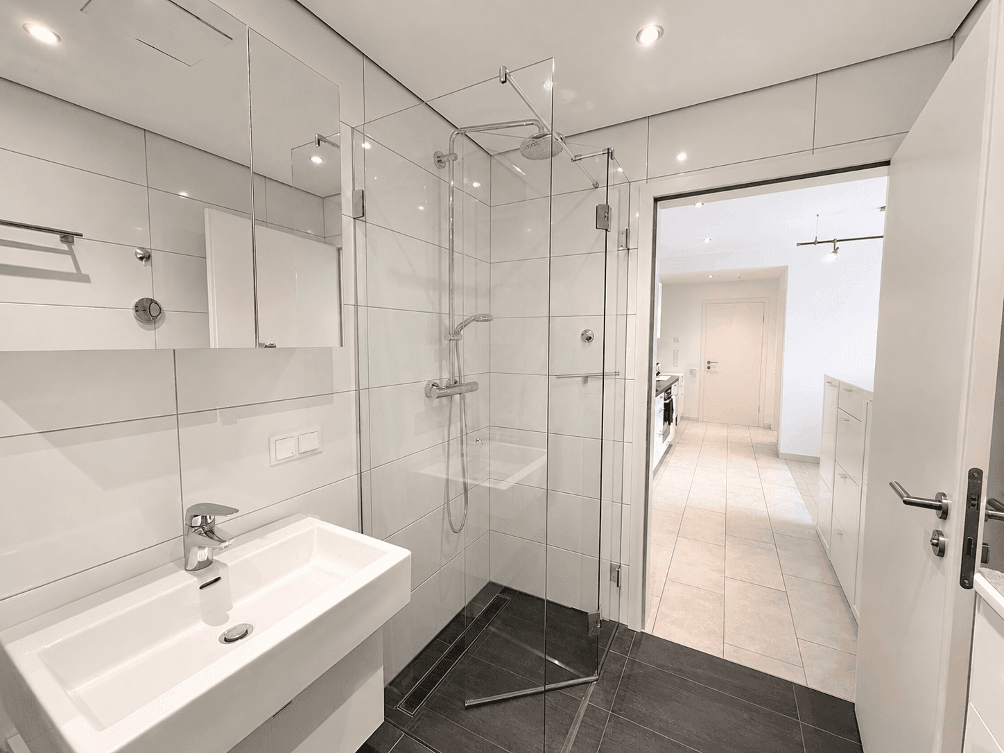 Modernes Badezimmer mit begehbarer Dusche, weißen Fliesen und Einzelwaschbecken.