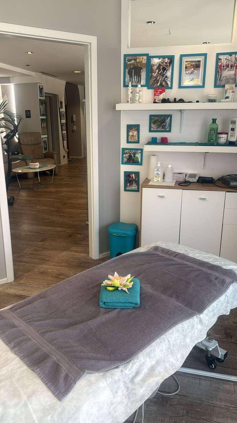 Behandlungsraum mit Massageliege und Blick in einen angrenzenden Bereich mit Regalen und Produkten.