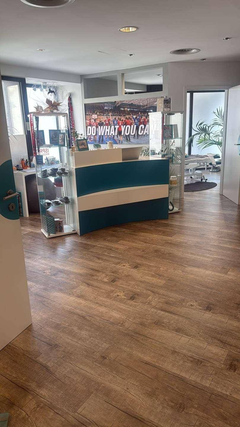 Empfangsbereich mit Rezeption, Sitzgelegenheiten und Fitnessgeräten, offen gestaltet mit Holzoptikboden.