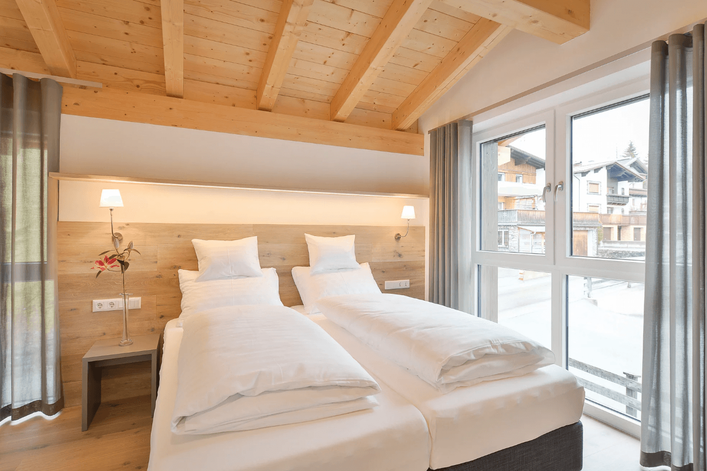 Gemütliches Schlafzimmer mit Holzbalkendecke, zwei Einzelbetten und Blick auf die verschneite Landschaft.