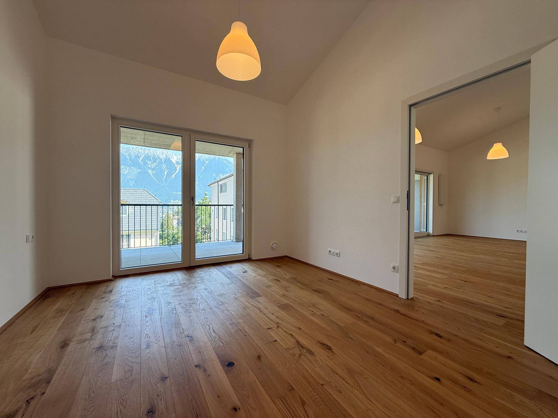 Helles Schlafzimmer mit Holzboden, Balkonzugang und beeindruckendem Bergblick.