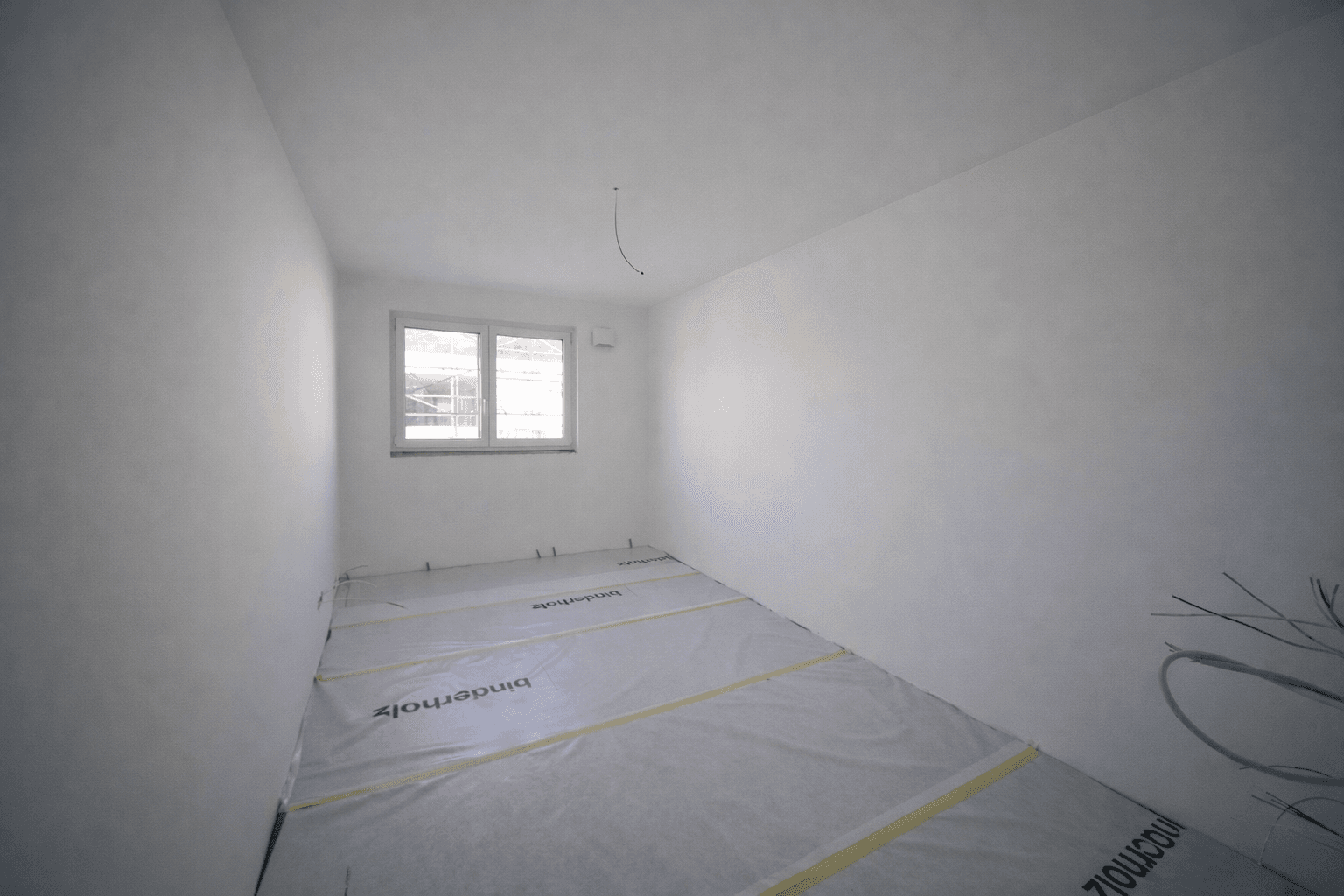 Kleineres Schlafzimmer im Rohbau mit Fenster und Blick auf die Baustelle.