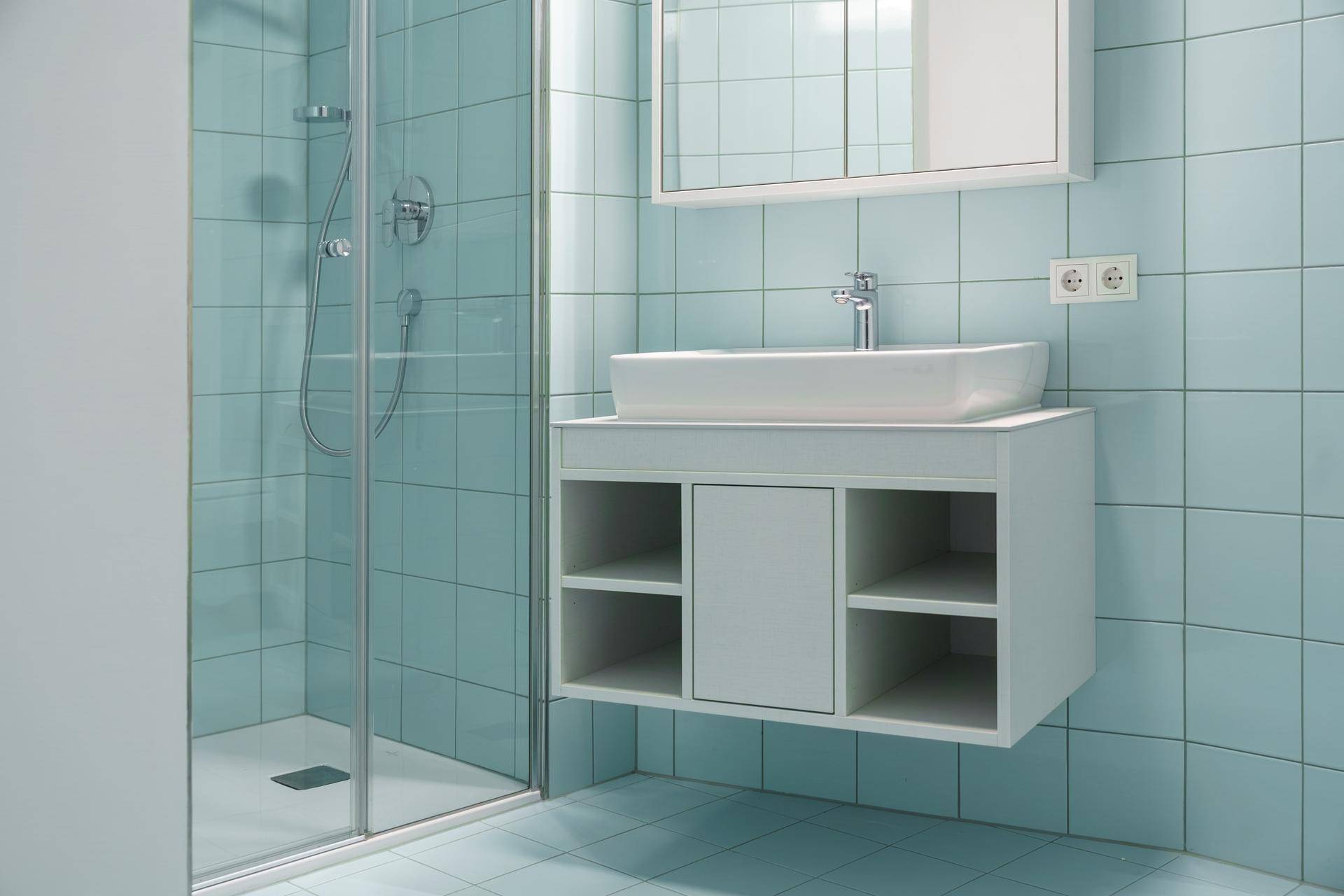 Modernes Badezimmer mit hellblauen Fliesen, Waschtisch und begehbarer Dusche.