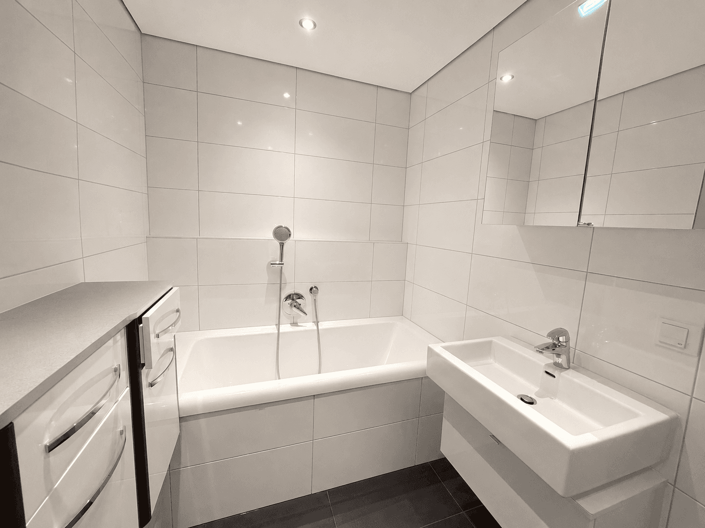Helles Badezimmer mit Badewanne, Einzelwaschbecken und weißen Wandfliesen.