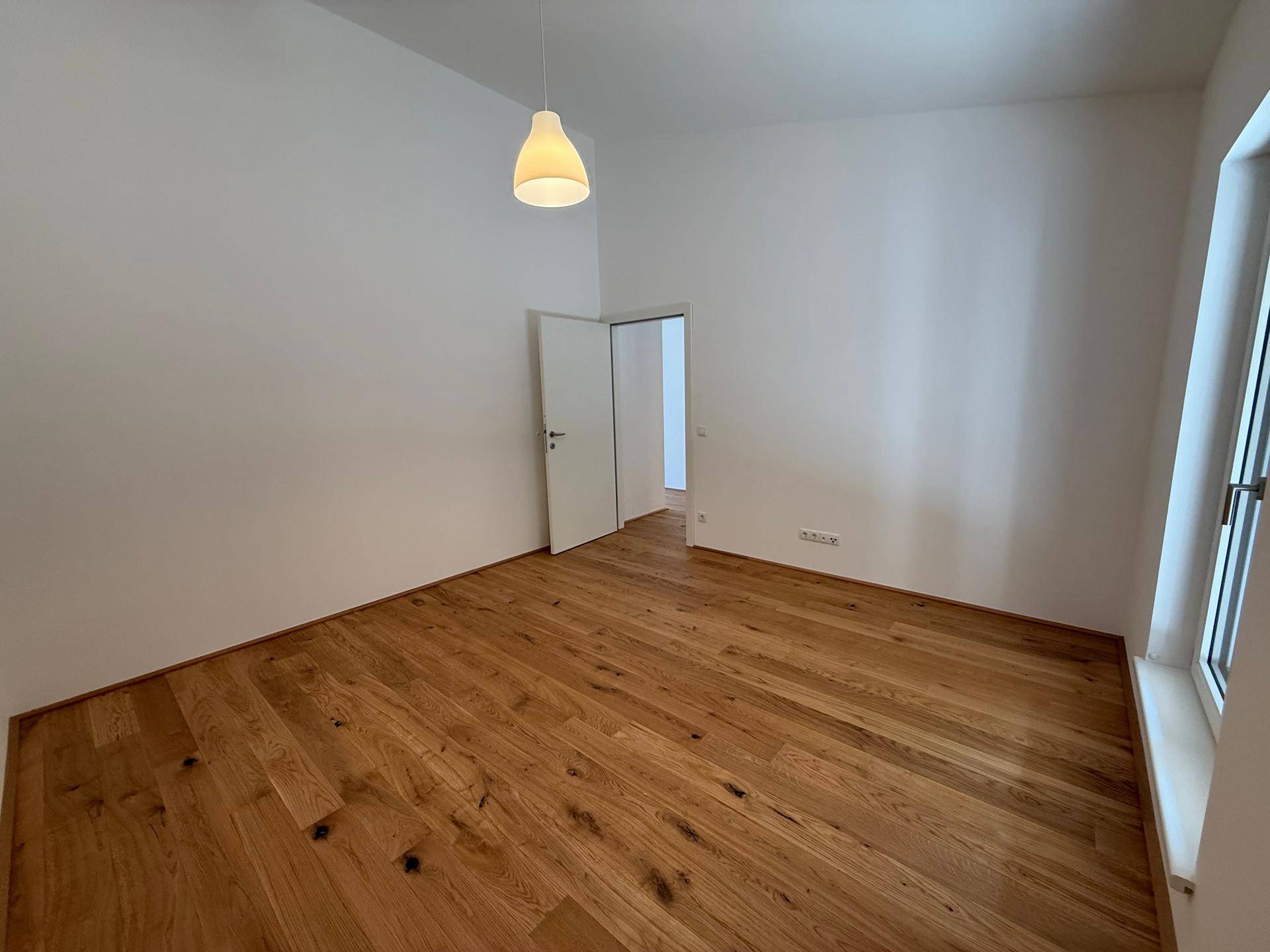 Helles Zimmer mit Holzdielenboden, weißen Wänden und einem Fenster für viel Tageslicht.