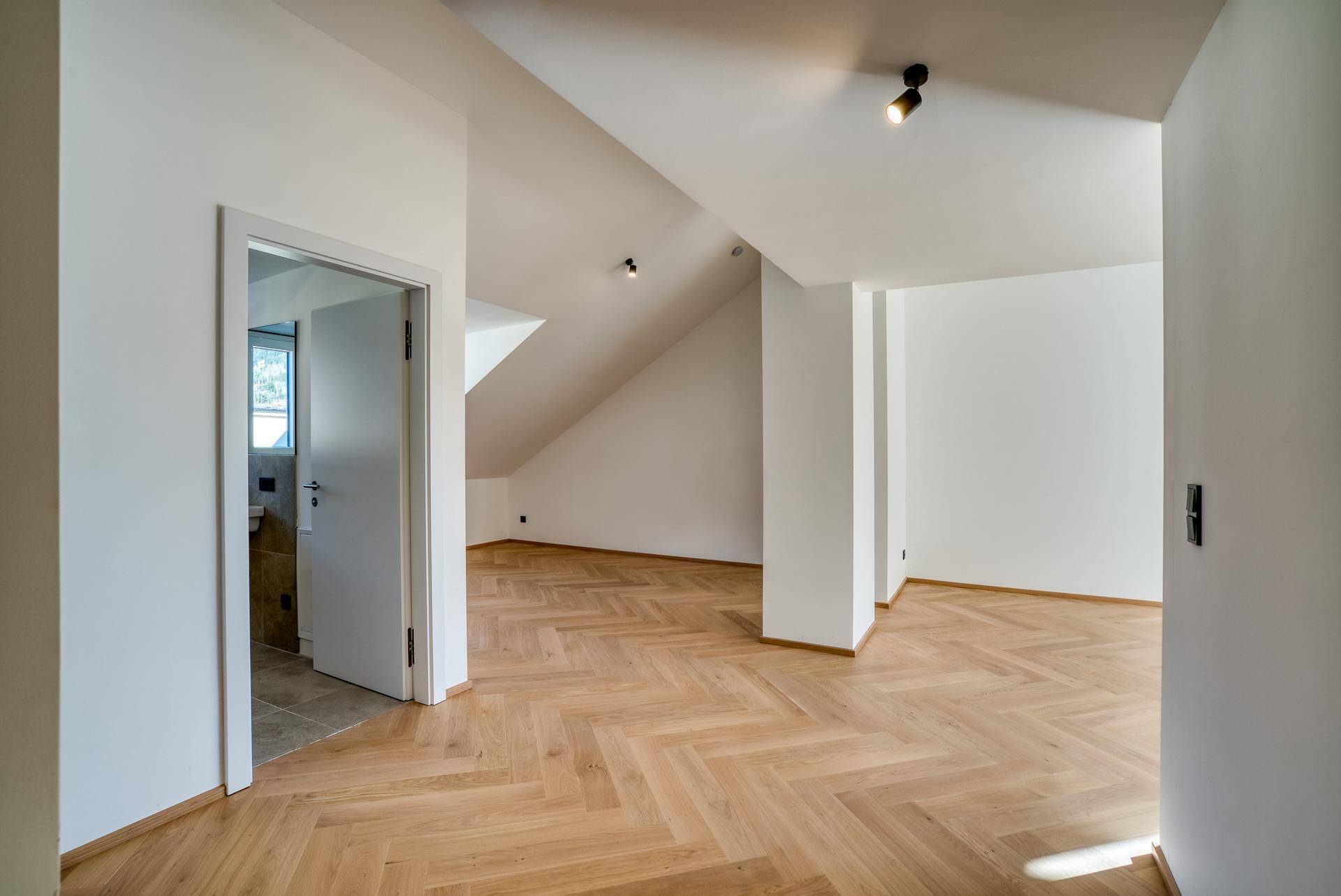 Heller, leerer Raum mit Fischgrätparkett und Zugang zu einem Badezimmer.