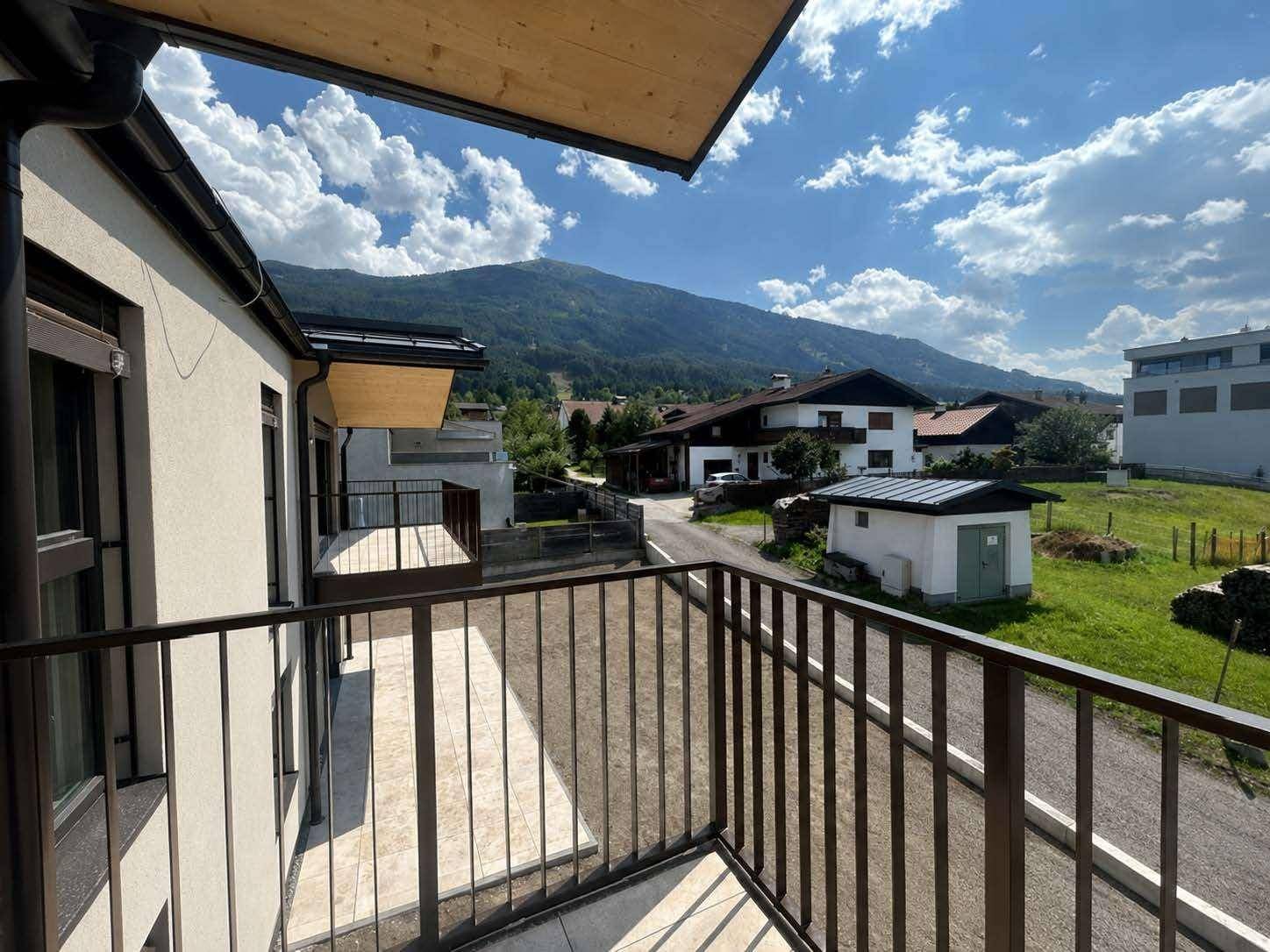 Balkon mit Metallgeländer und Ausblick auf die grüne Umgebung und Berge.