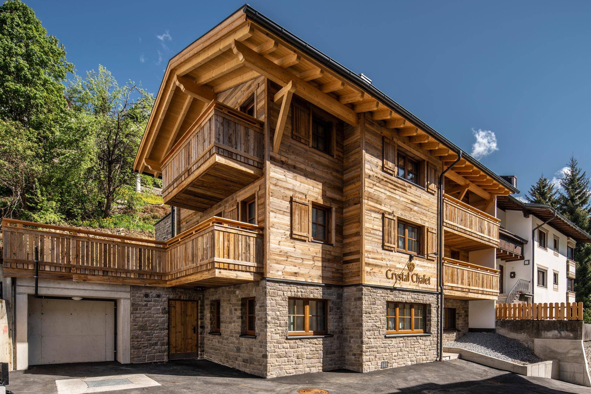Modernes Holzchalet mit Steinsockel und Balkonen unter blauem Himmel im Sommer.