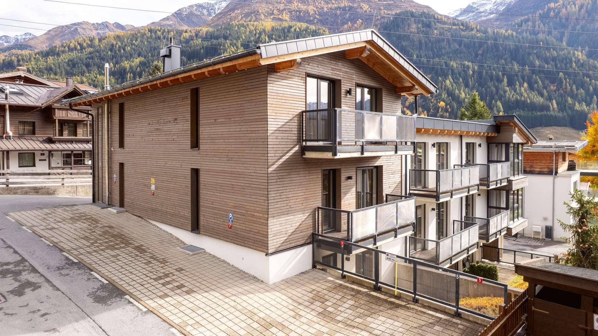 Seitenansicht des modernen Gebäudes mit Holzfassade, Balkonen und Bergblick.