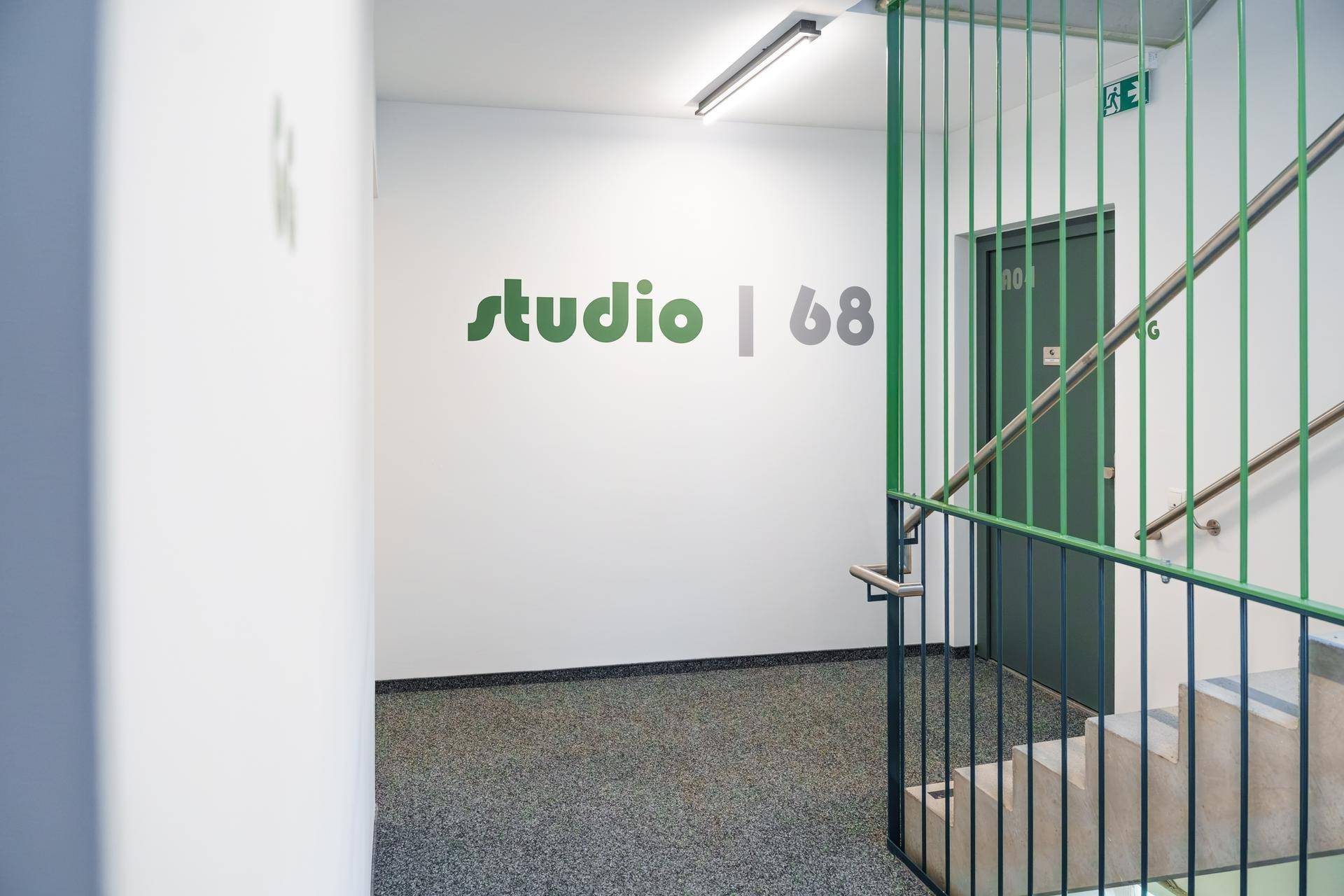 Heller Flurbereich mit Treppe, grünem Geländer und Beschilderung zu den Studios.