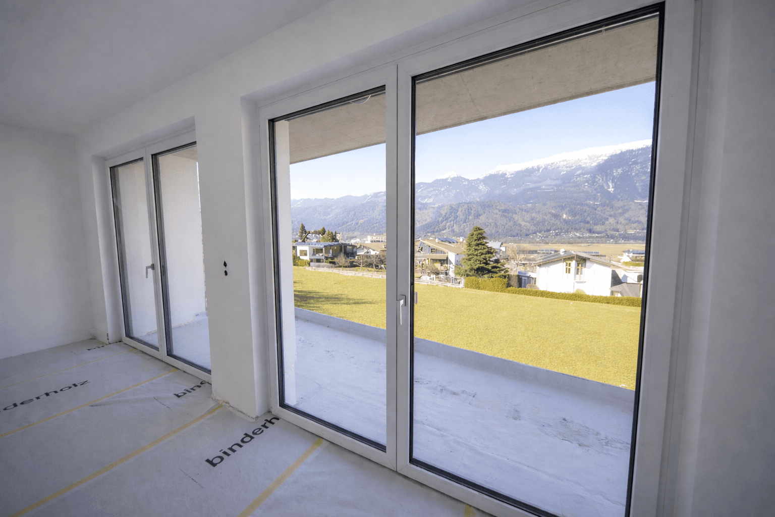 Geräumiger Wohnbereich im Rohbau mit großen Schiebetüren und beeindruckendem Bergblick.
