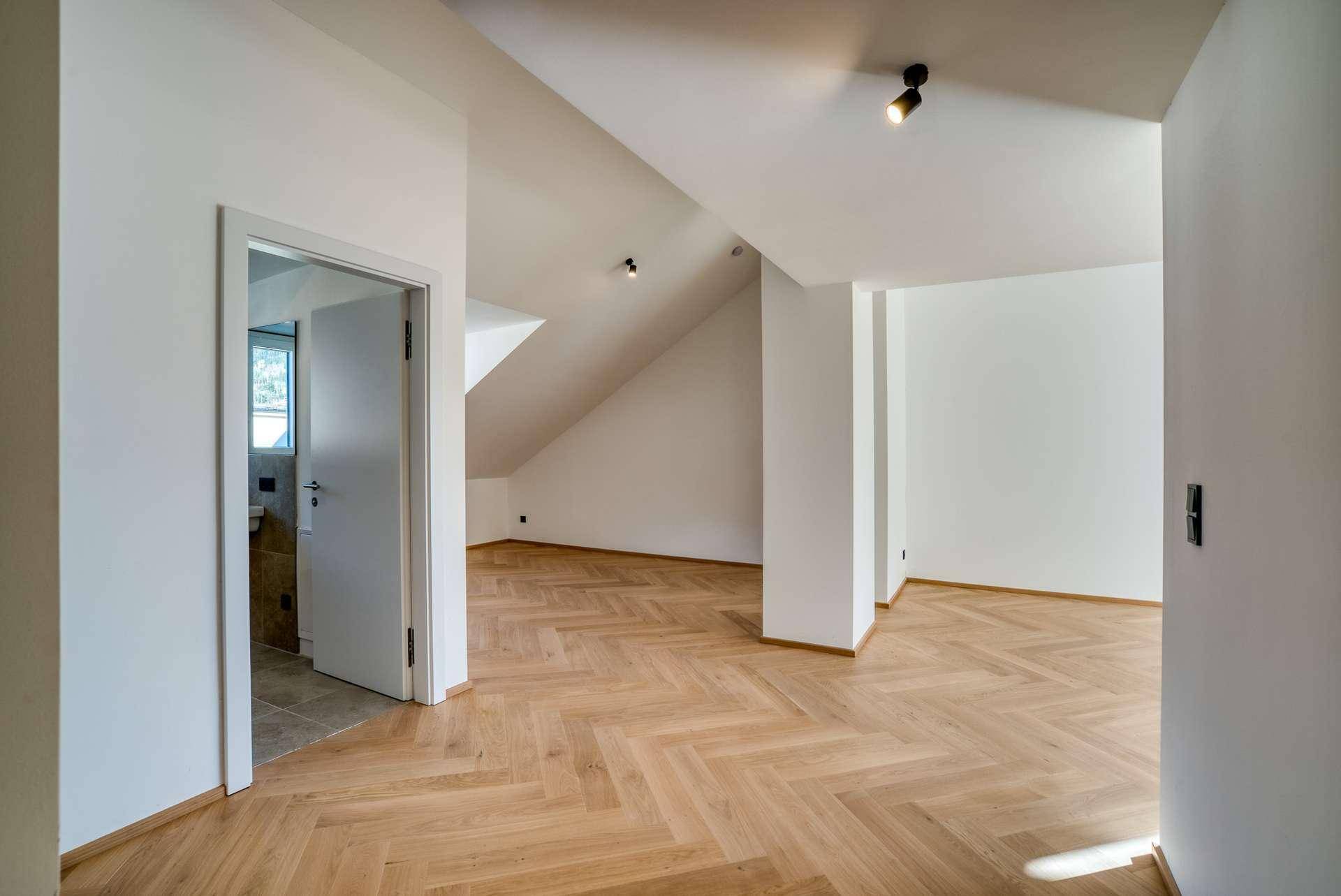 Geräumiger, unmöblierter Raum mit Fischgrätparkett und Zugang zu einem Badezimmer.