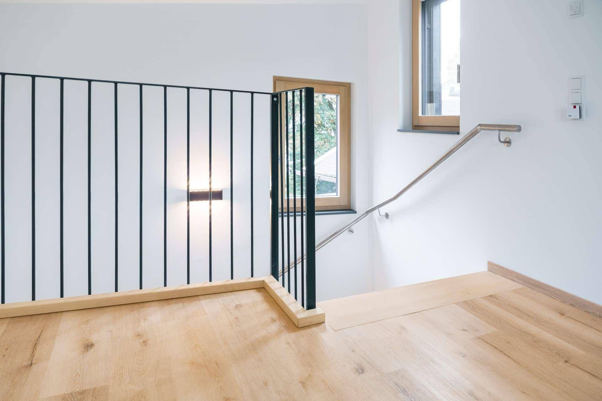 Heller Treppenabsatz mit Holzfußboden, modernem Geländer und Fenster.