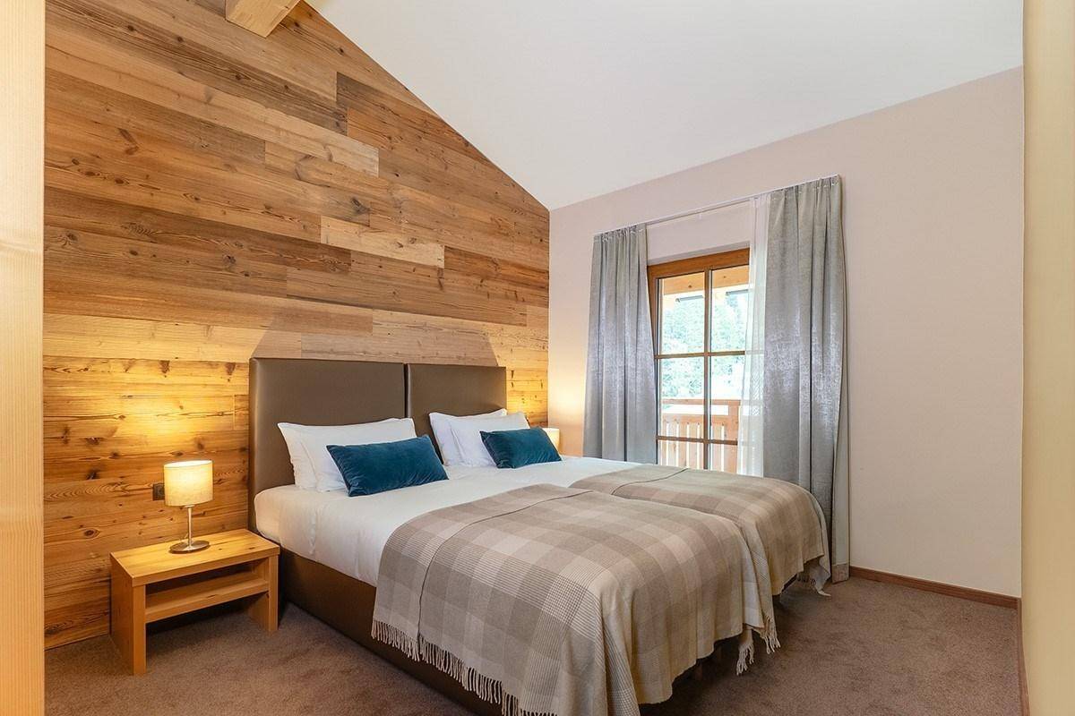 Schlafzimmer mit zwei Einzelbetten, Holzwand und Blick ins Grüne durch das Fenster.