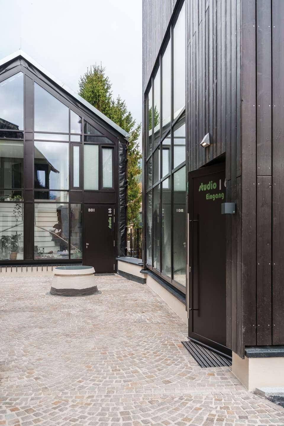 Eingangsbereich der modernen Gebäude mit dunkler Holzfassade und großen Glasfronten.