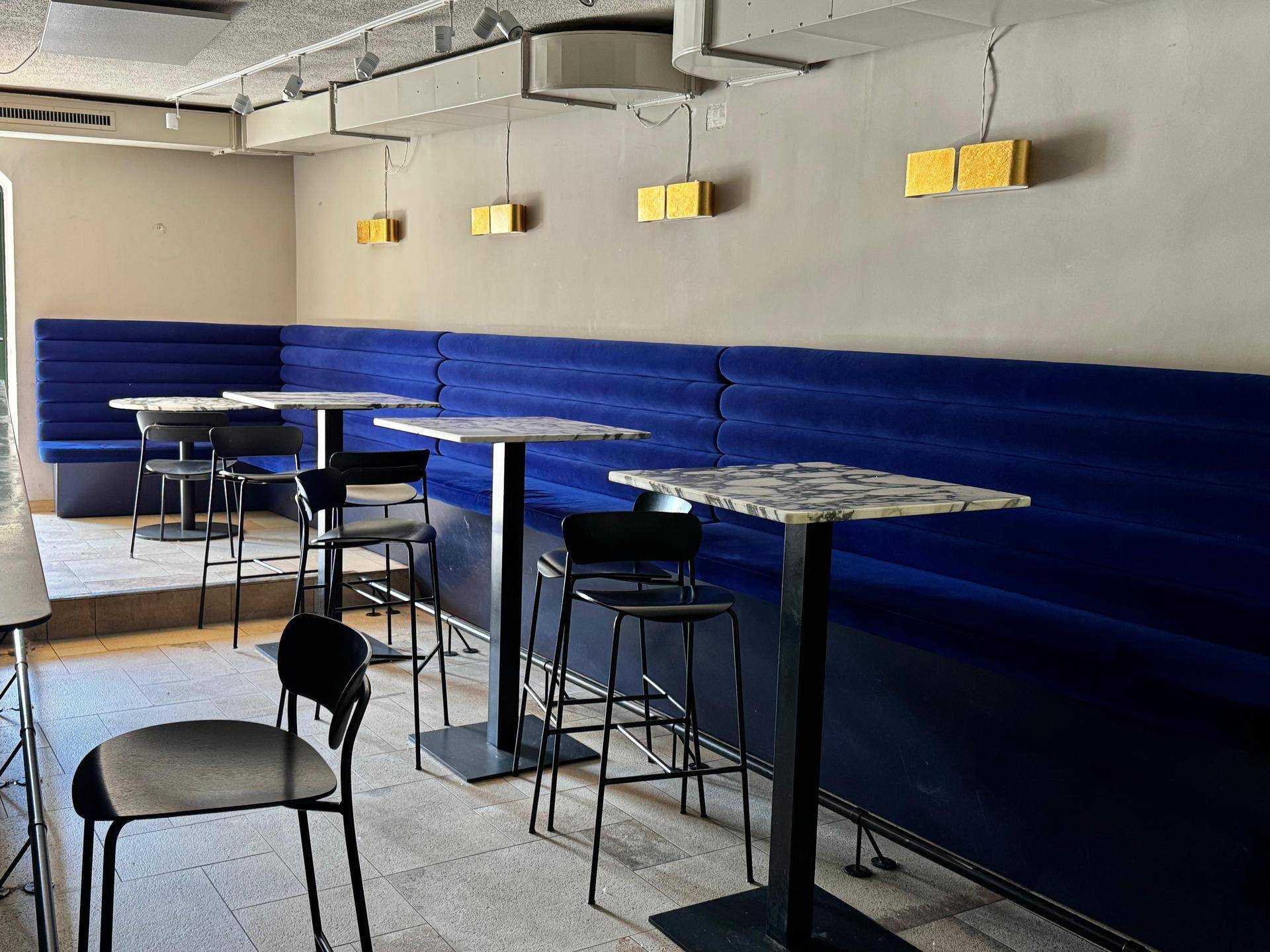 Moderner Barbereich mit blauen Polsterbänken, hohen Stehtischen und Marmorplatten in einem Café.