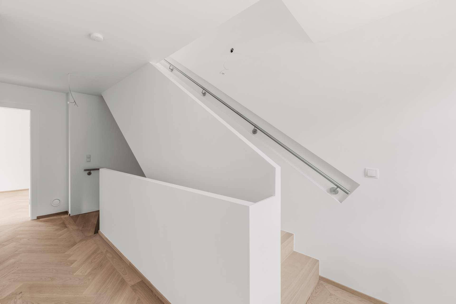 Moderne Treppe mit Holzstufen und minimalistischem Geländer in hellem Flur.