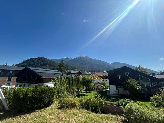 Weitläufiger Blick auf die grüne Landschaft und die beeindruckende Bergkulisse unter strahlend blauem Himmel.