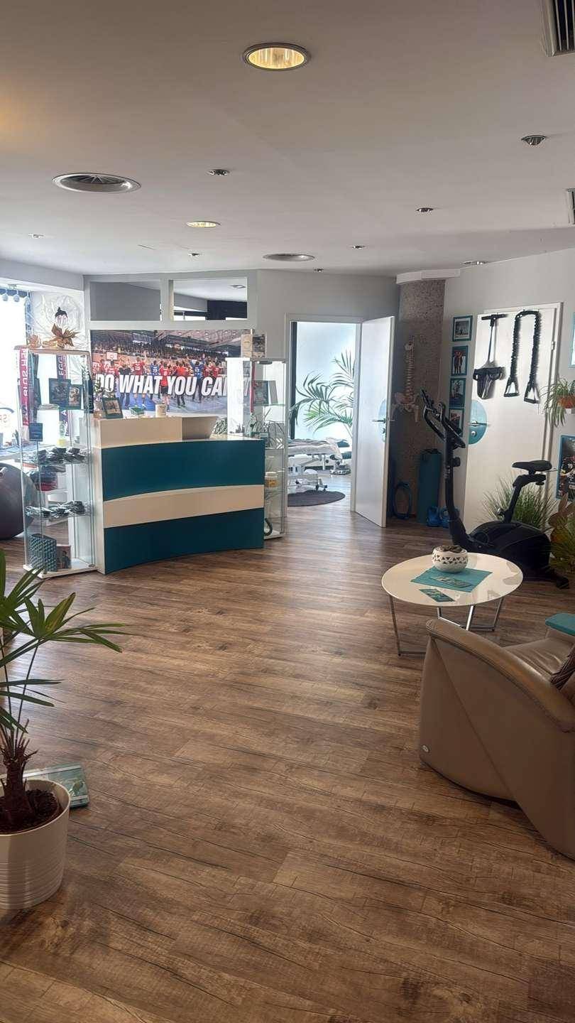 Empfangsbereich mit Rezeption, Sitzgelegenheiten und Fitnessgeräten, offen gestaltet mit Holzoptikboden.