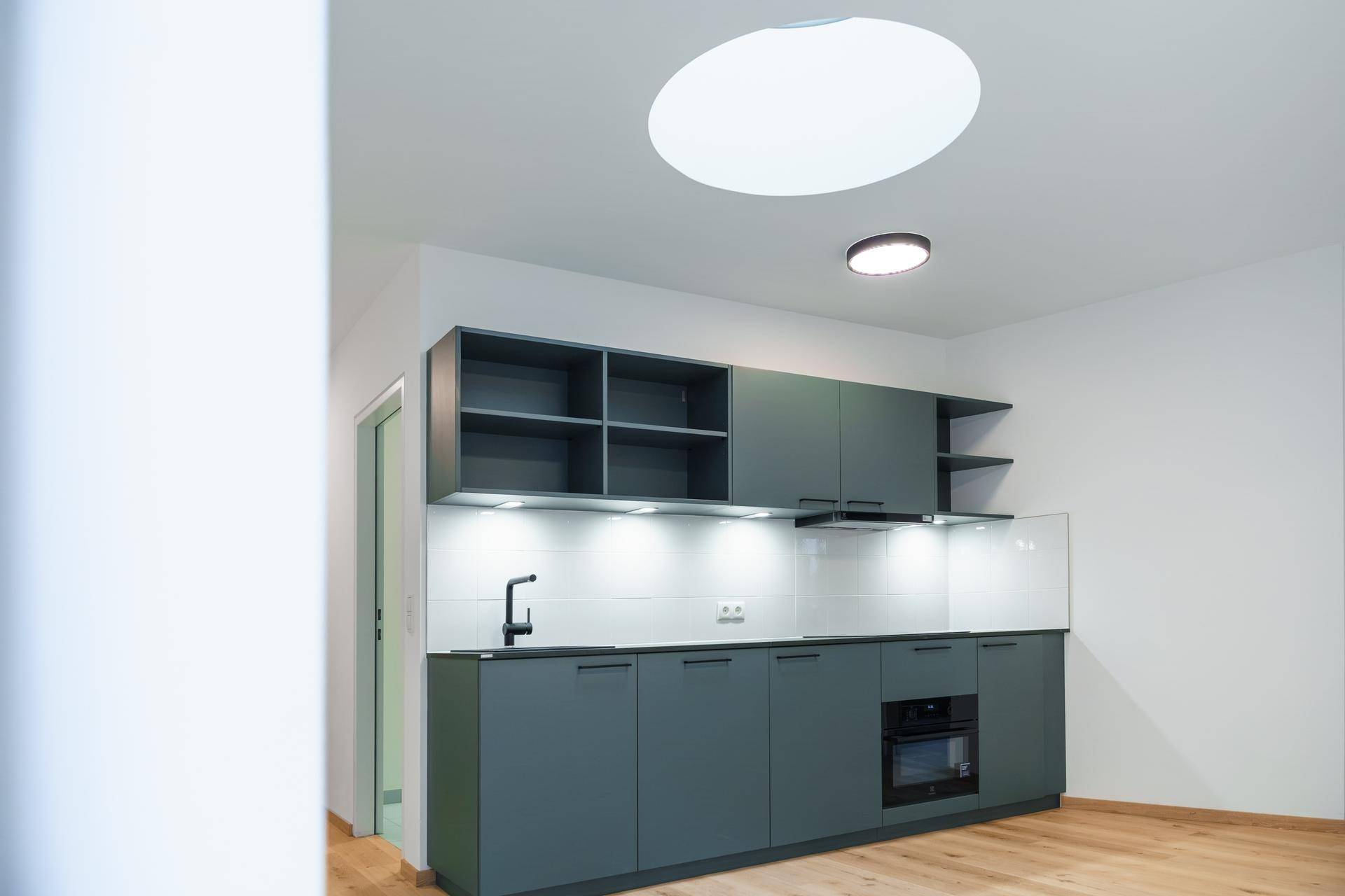 Moderne Küchenzeile in hellem Raum mit Oberlicht, grauen Schränken und Holzfußboden.