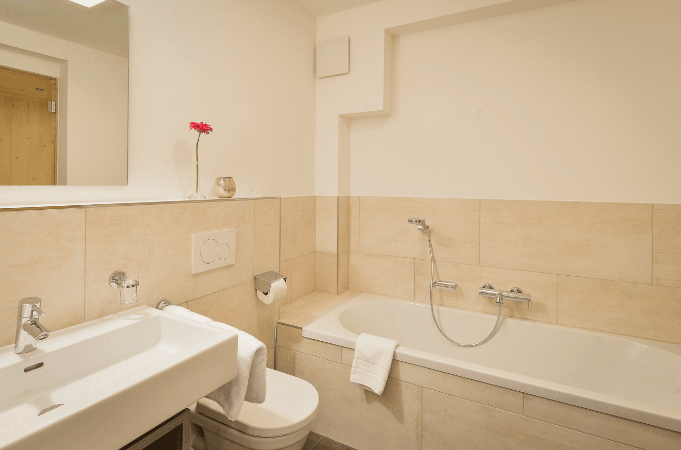 Helles Badezimmer mit Badewanne, WC und modernem Waschbecken in beigen Fliesen.