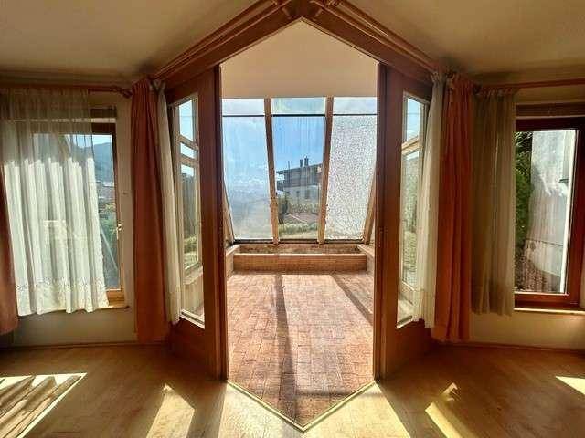 Blick aus einem Innenraum in einen hellen Wintergarten mit großen Glasflächen und Fliesenboden.
