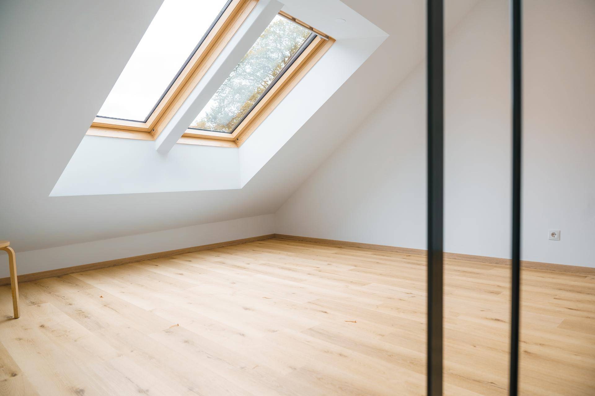 Heller Raum mit Dachschrägen, Holzfußboden und großem Dachfenster.