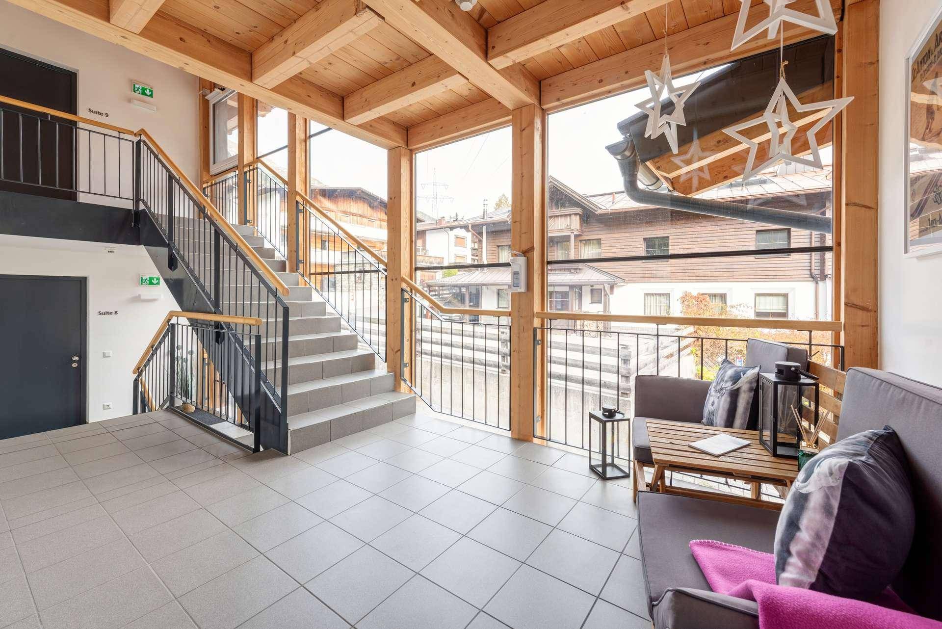Heller Eingangsbereich mit Treppe, großen Fenstern und Sitzgelegenheiten.