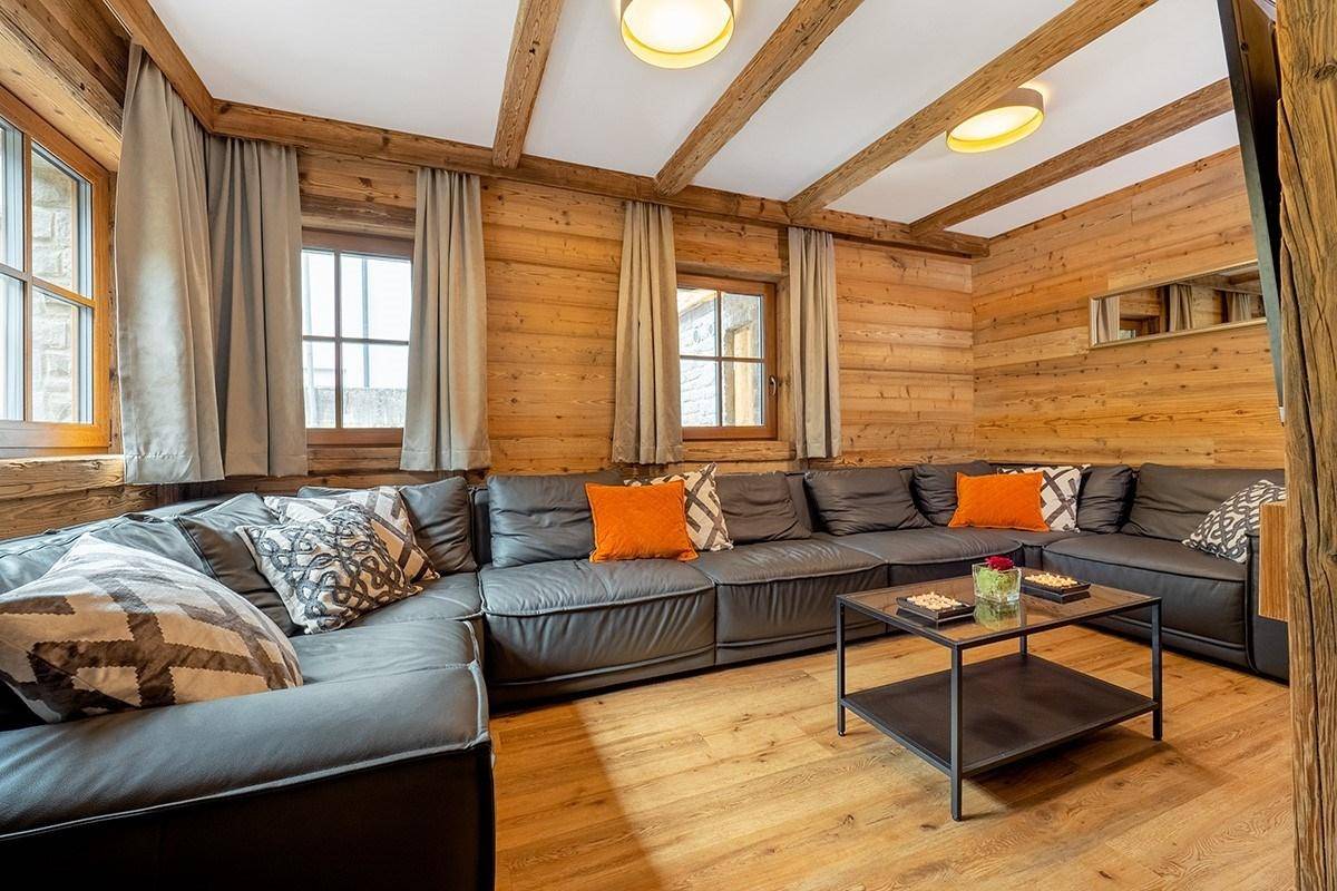 Gemütliches Wohnzimmer mit großer Eckcouch, Holzwänden und sichtbaren Deckenbalken.