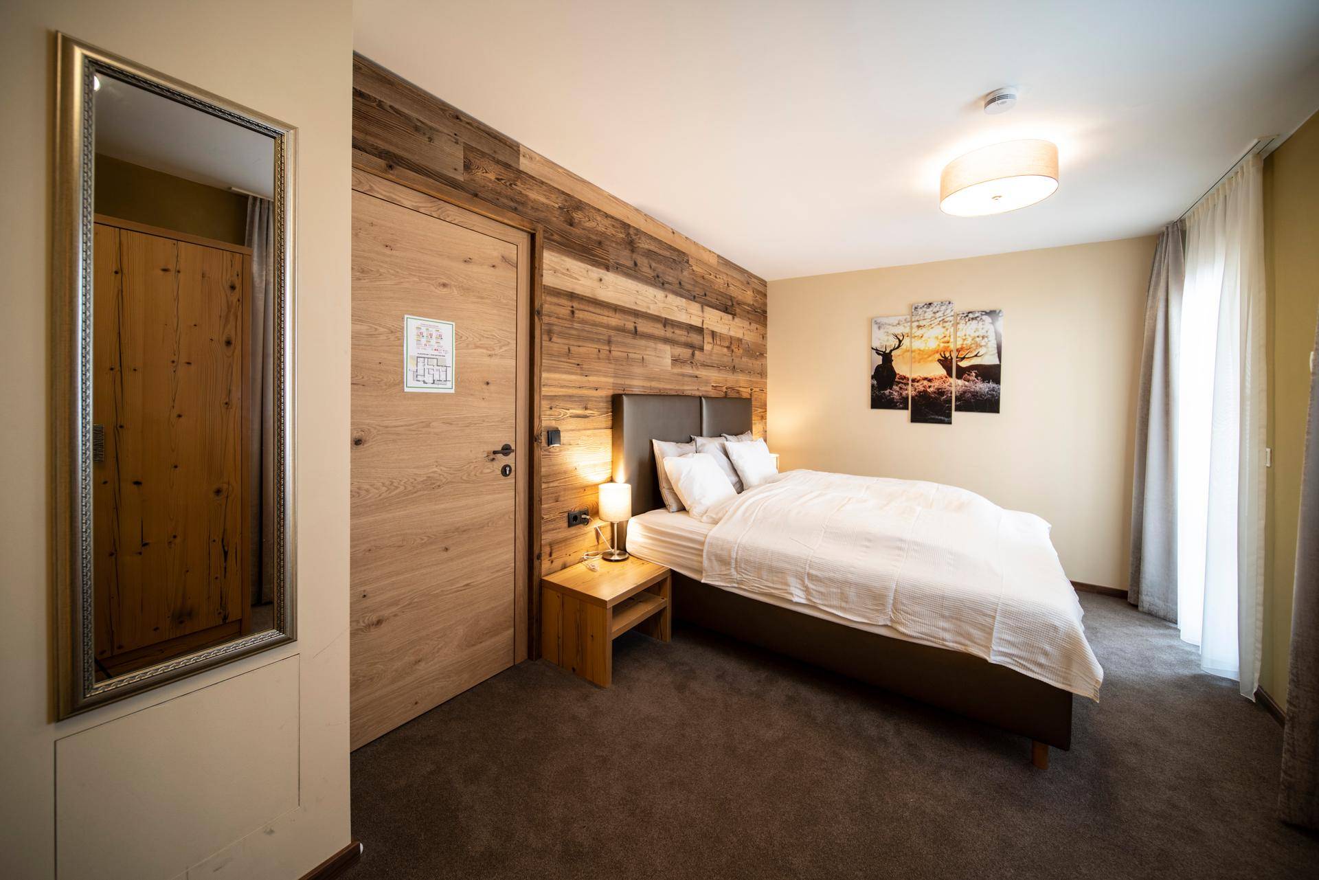 Schlafzimmer mit Doppelbett, Holzakzentwand und Teppichboden, modern eingerichtet.